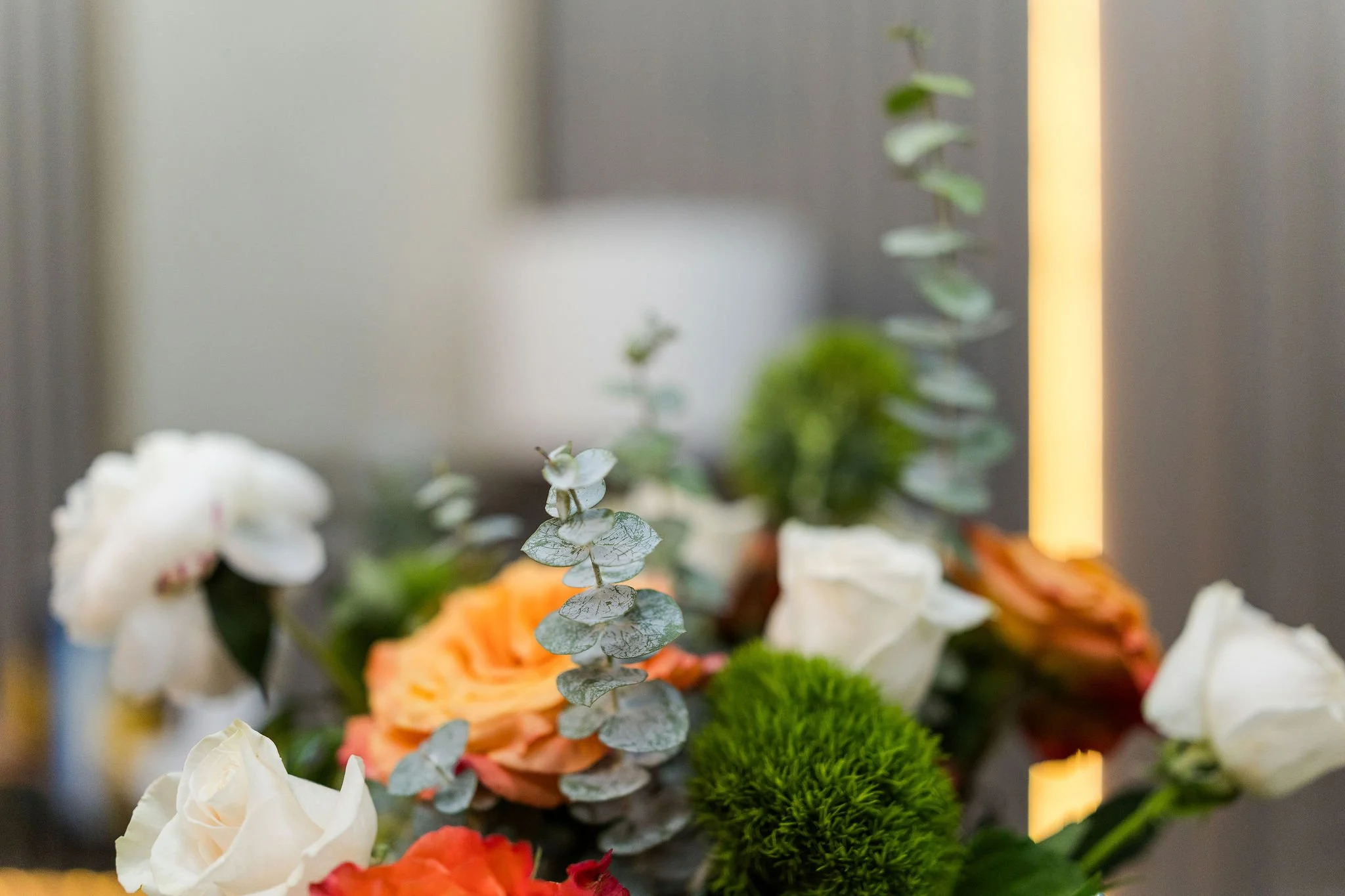 Close-up of a floral arrangement with eucalyptus leaves, roses, and other flowers in the background, with a soft blurred background.