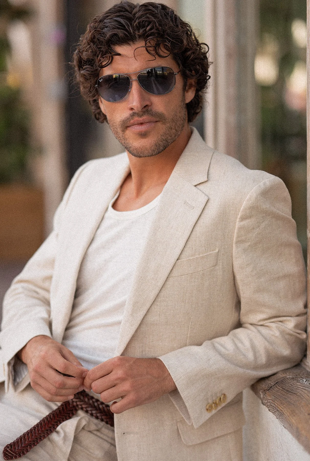 Man in white blazer and sunglasses sitting outdoors, looking at camera. Photographed by Fashion, resort, swimwear, luxury lifestyle photographer, Kelly Fajack.