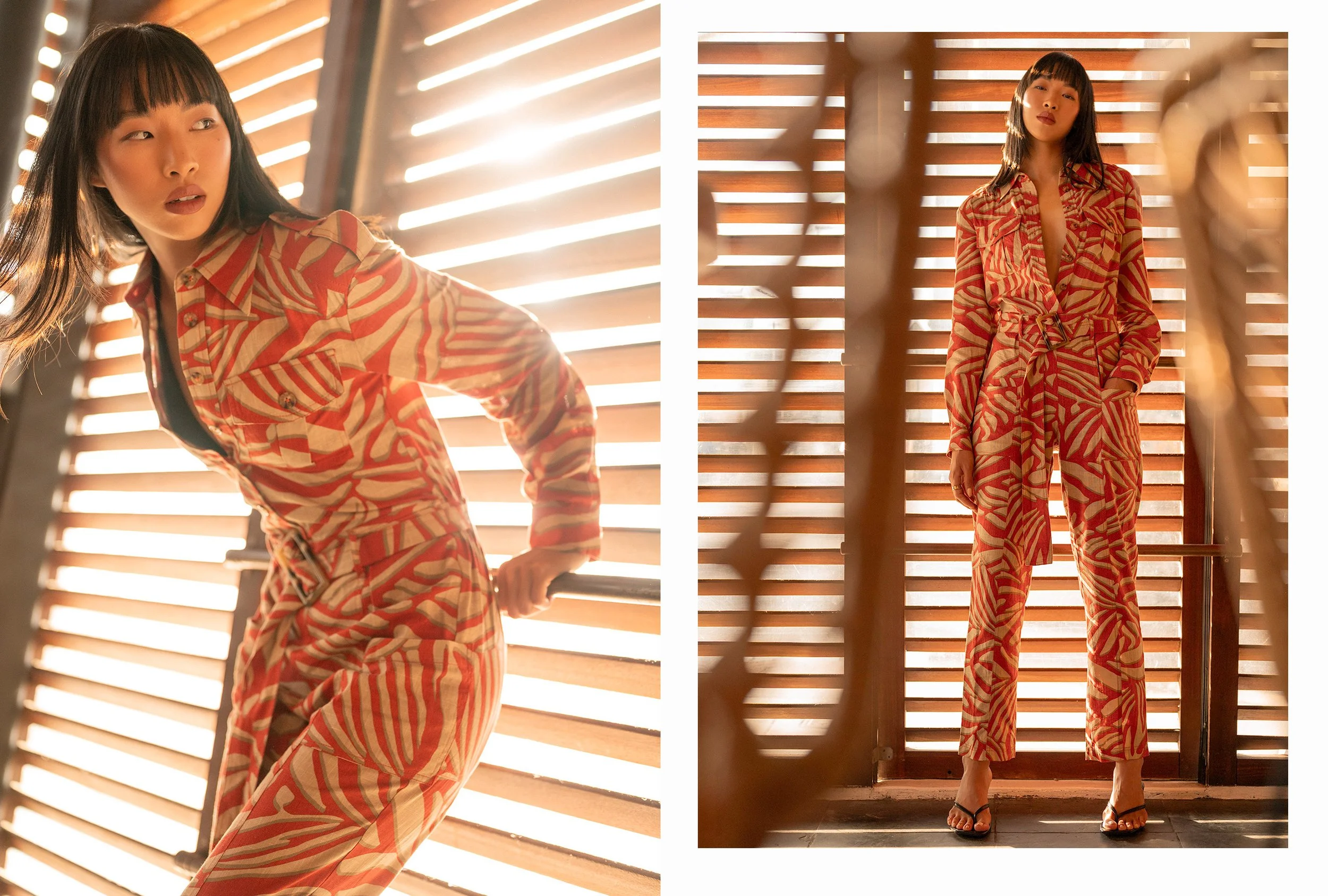 A woman in a matching red and tan patterned blazer and pants standing in front of wooden blinds, illuminated by warm sunlight.