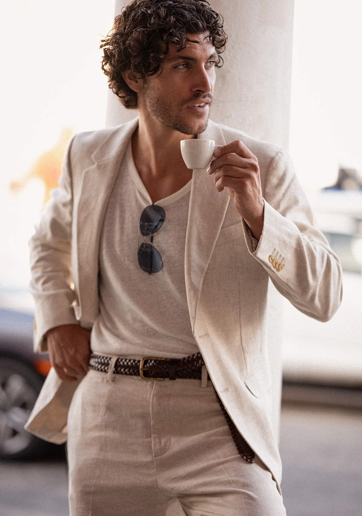 A man with curly hair dressed in a beige suit, holding a small white cup, standing outdoors in a city. Photographed by Fashion, resort, swimwear, luxury lifestyle photographer, Kelly Fajack.