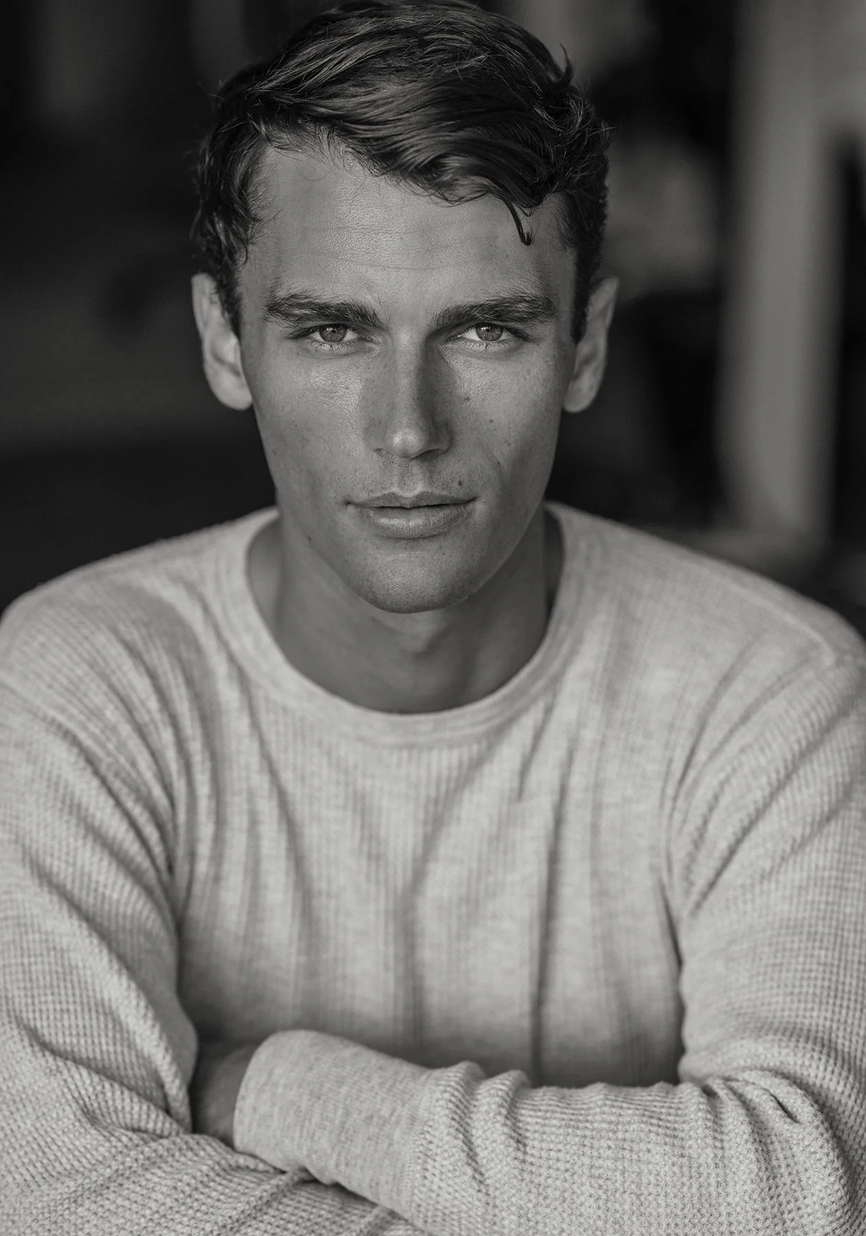 Black and white portrait of a young man with light skin and wavy hair, wearing a light-colored sweater, looking directly at the camera.