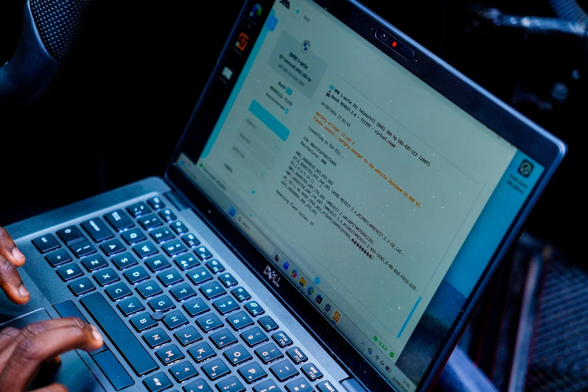 Close-up of a person's hand typing on a laptop keyboard with a focus on the screen displaying a vehicle diagnostic or coding software.