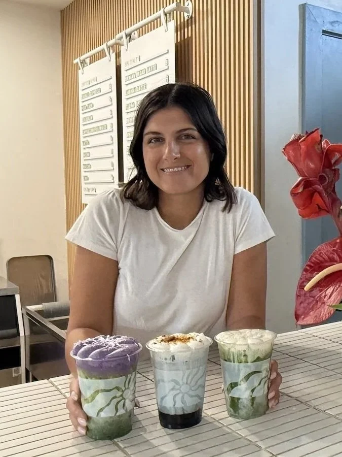 A woman sitting at a counter with three colorful layered drinks in front of her.