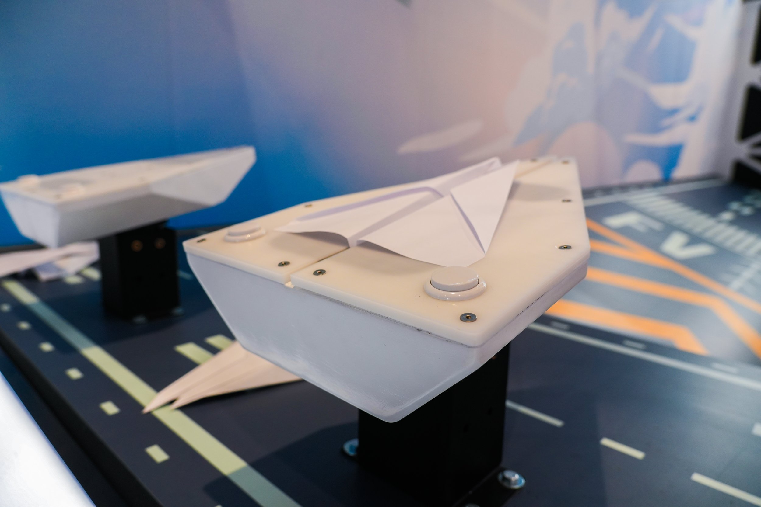 Close-up of a white mechanical device with a paper airplane model on top, set on a black surface with a printed road map beneath.