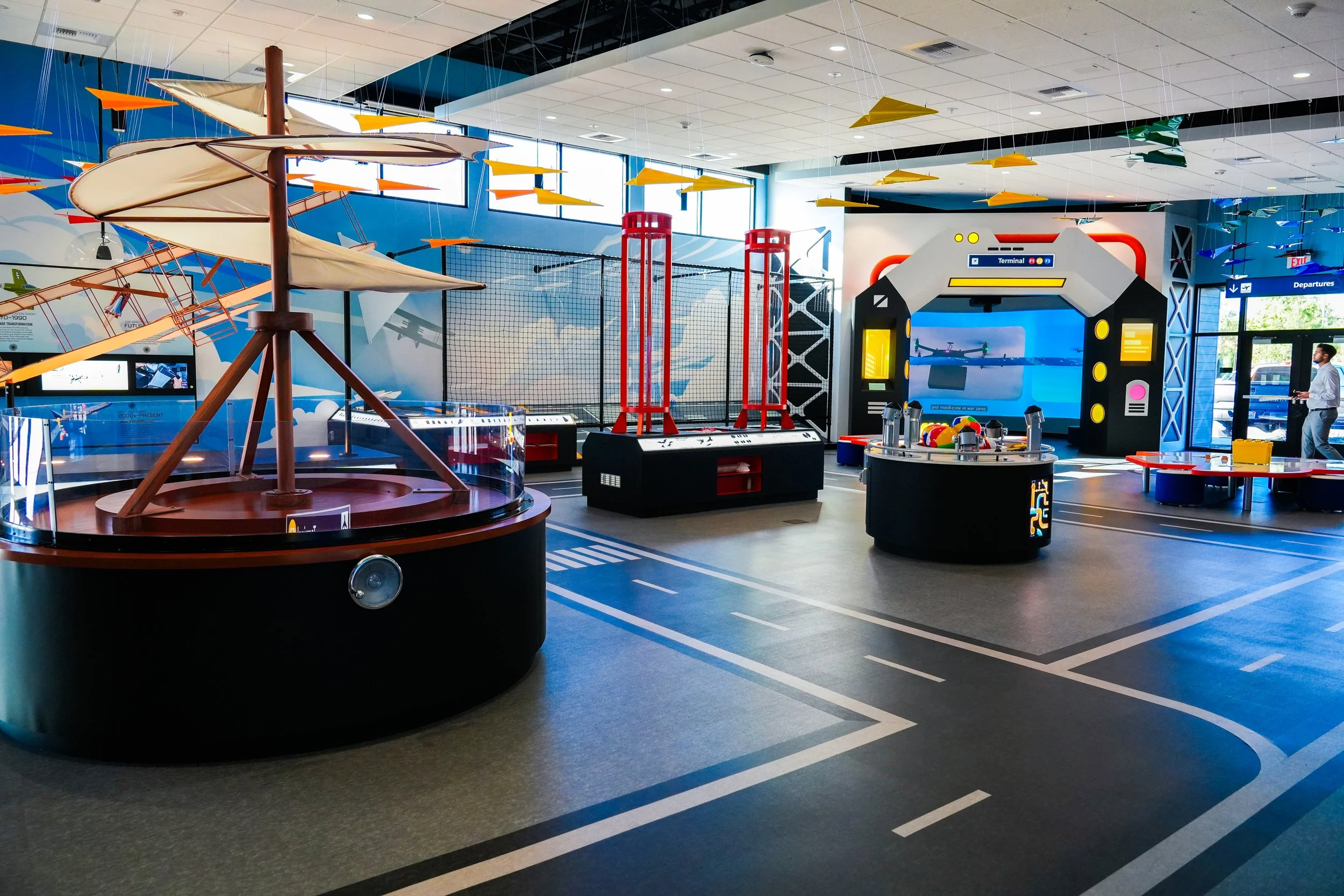 Indoor children's play area with airplane and space-themed decorations, including swings, climbing structures, and interactive screens.
