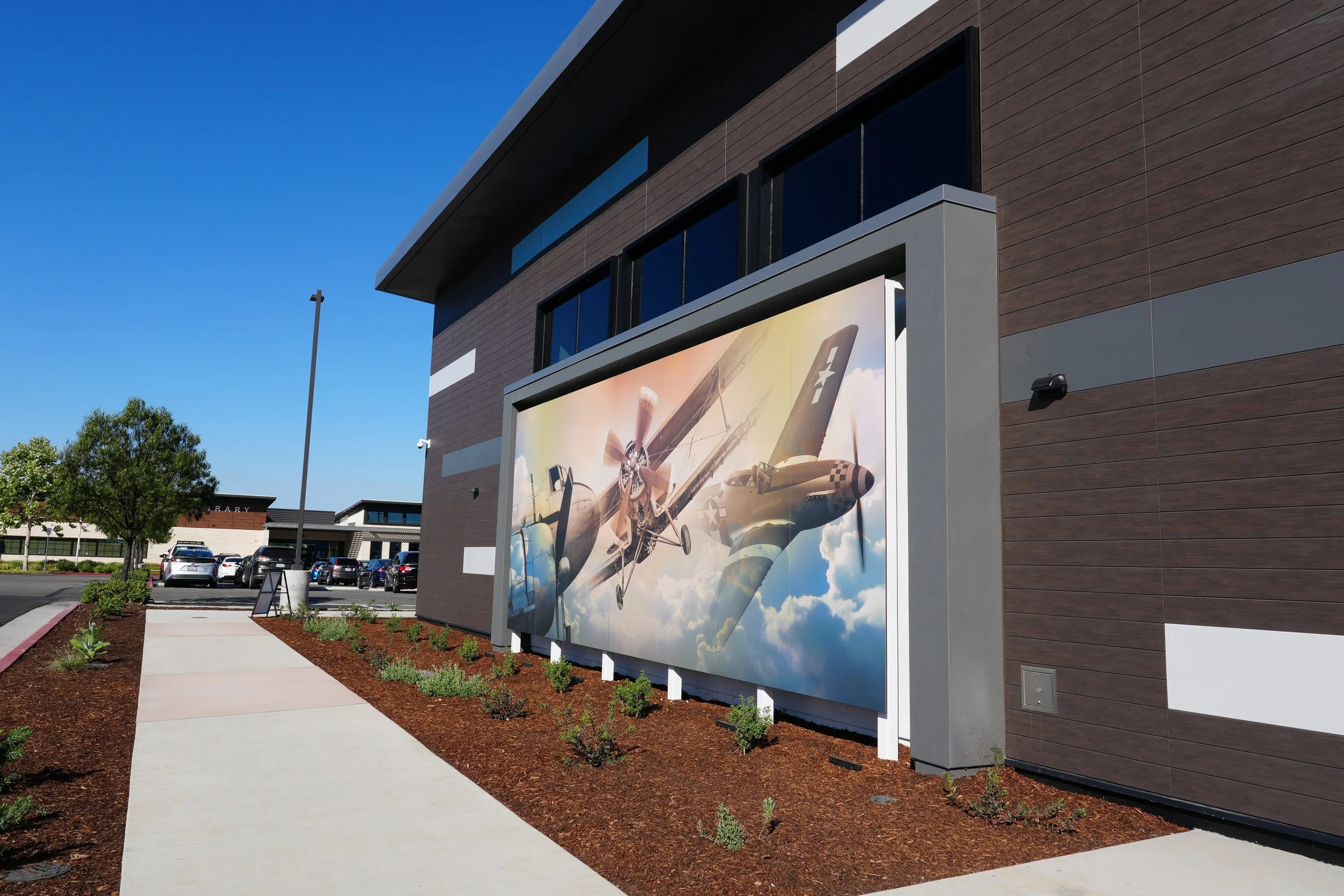 Modern building with large airplane artwork on billboard and parking lot with cars.