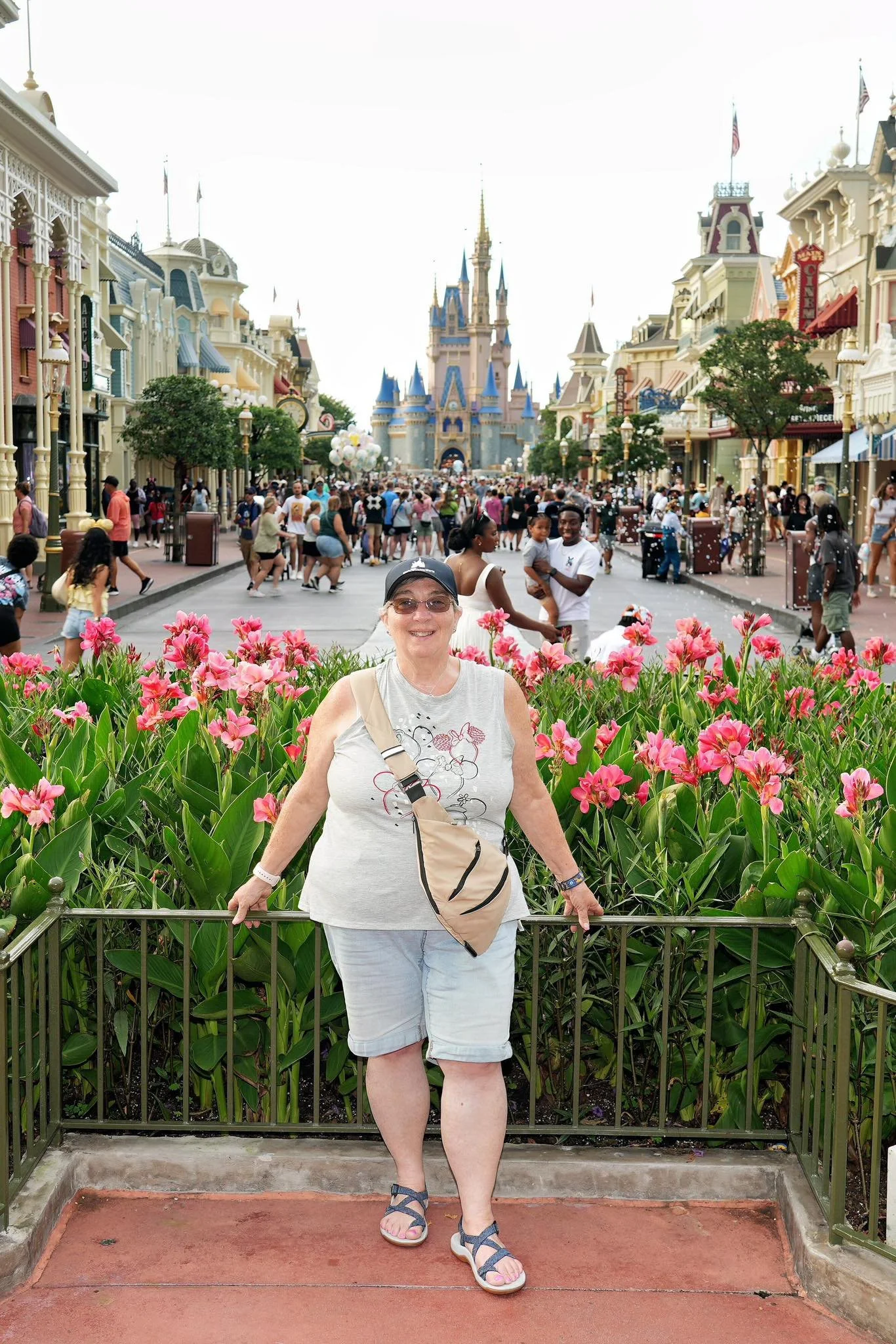 A woman standing and smiling in front of pink flowers at Disneyland with the Cinderella Castle in the background.