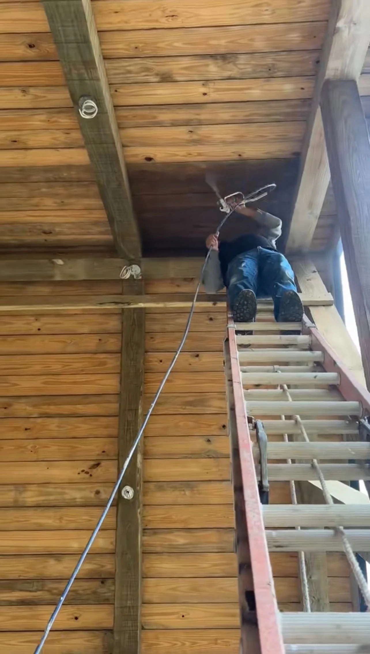 Professional painter using an airless sprayer to apply a protective transparent wood stain to a residential timber ceiling in Middle Tennessee.
