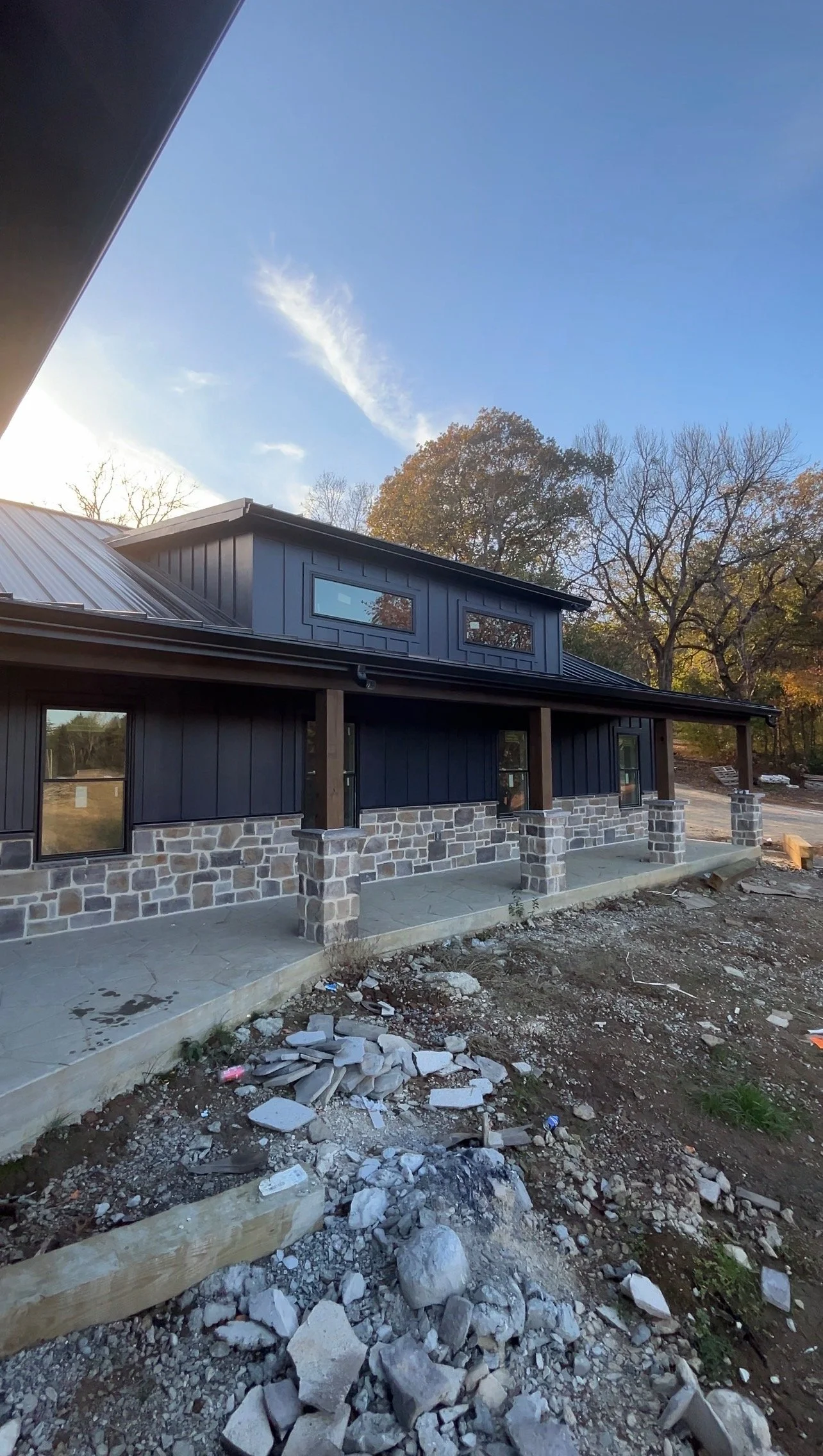 Before and after of a rustic home transformation featuring premium dark charcoal gray exterior board and batten siding painting above a stone facade in Middle Tennessee.