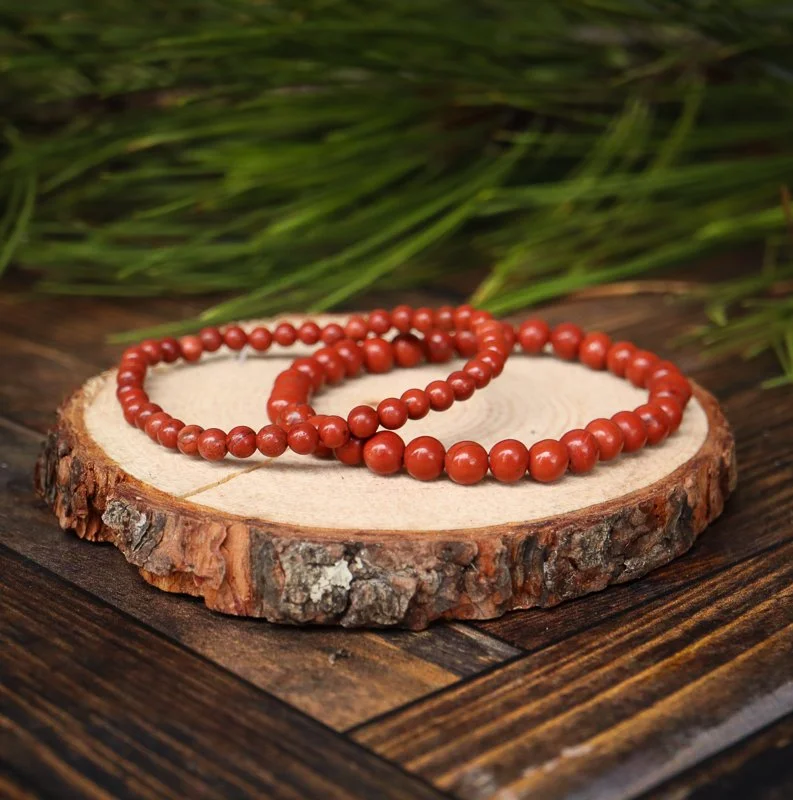 Two red beaded bracelets placed on a wooden cut of a tree trunk with greenery in the background.