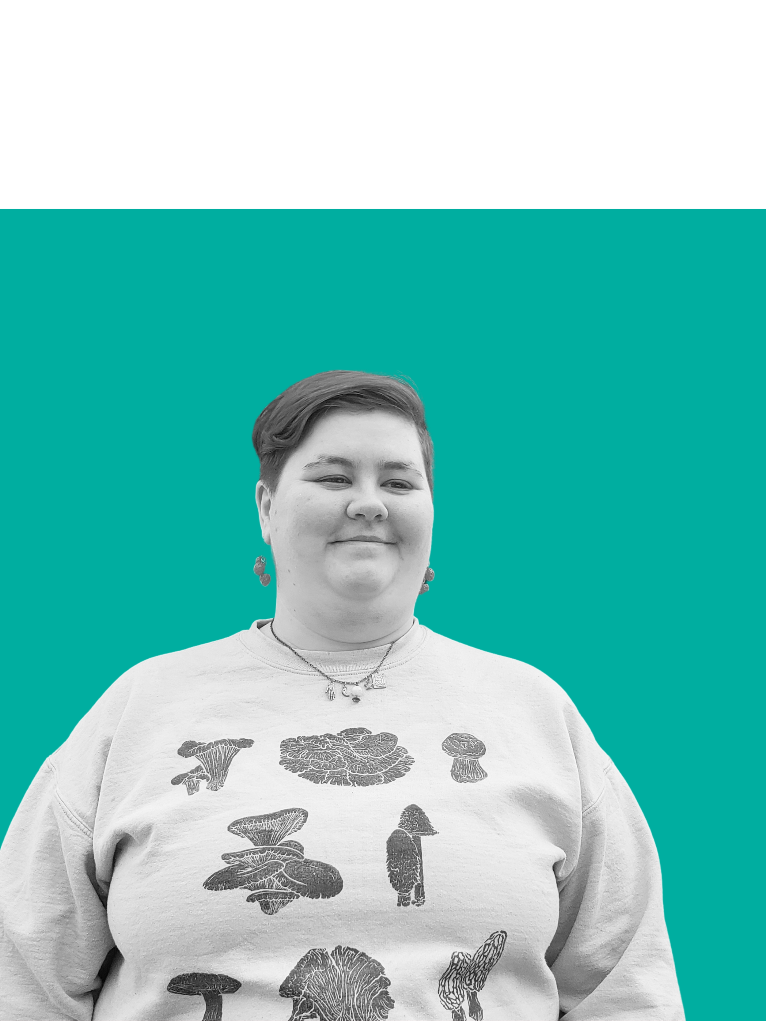 A young person with short hair and earrings, smiling, wearing a light-colored sweatshirt with mushroom illustrations, standing against a teal background.