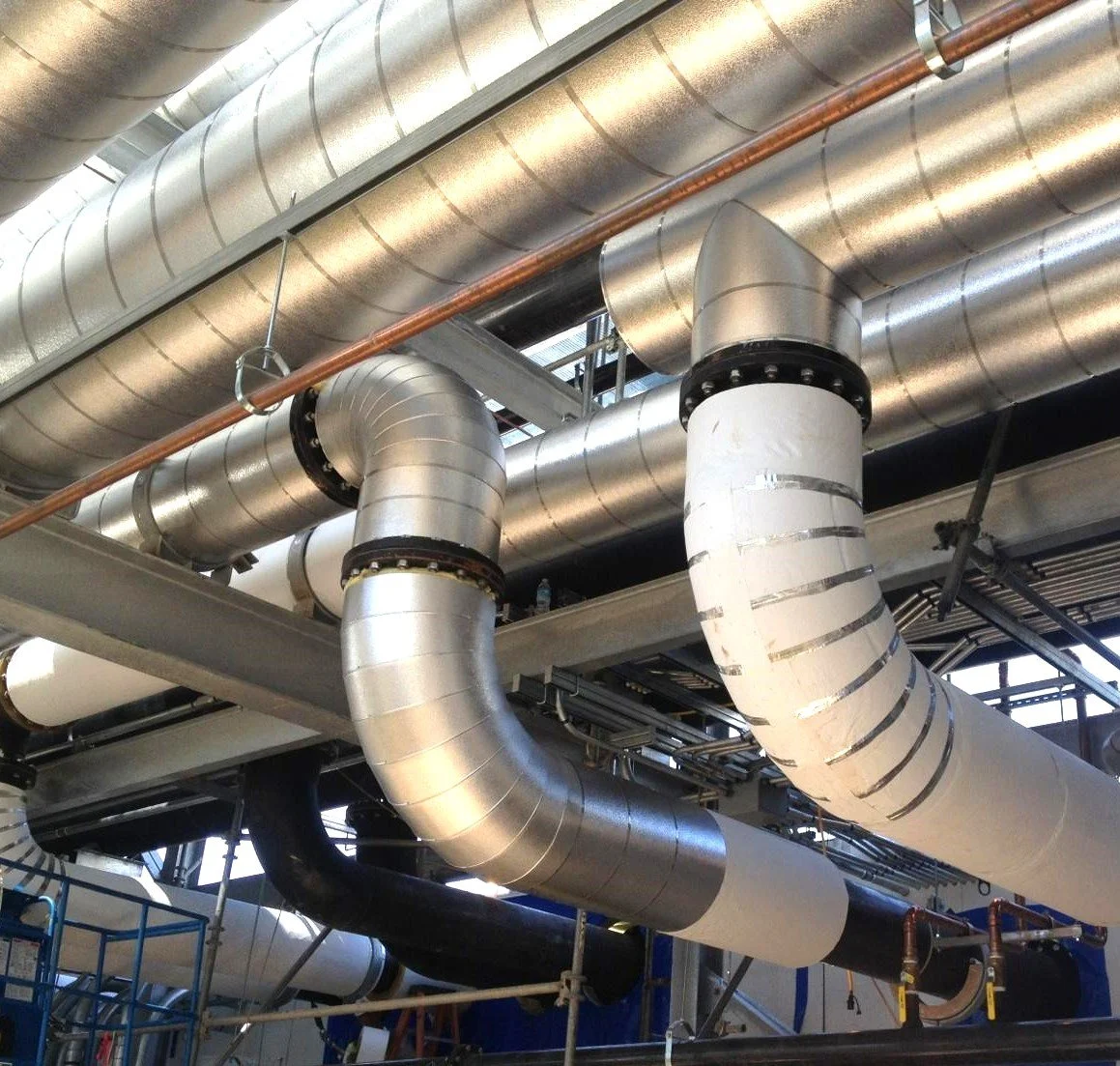 Industrial ductwork and piping system with metal and insulated pipes in a building.