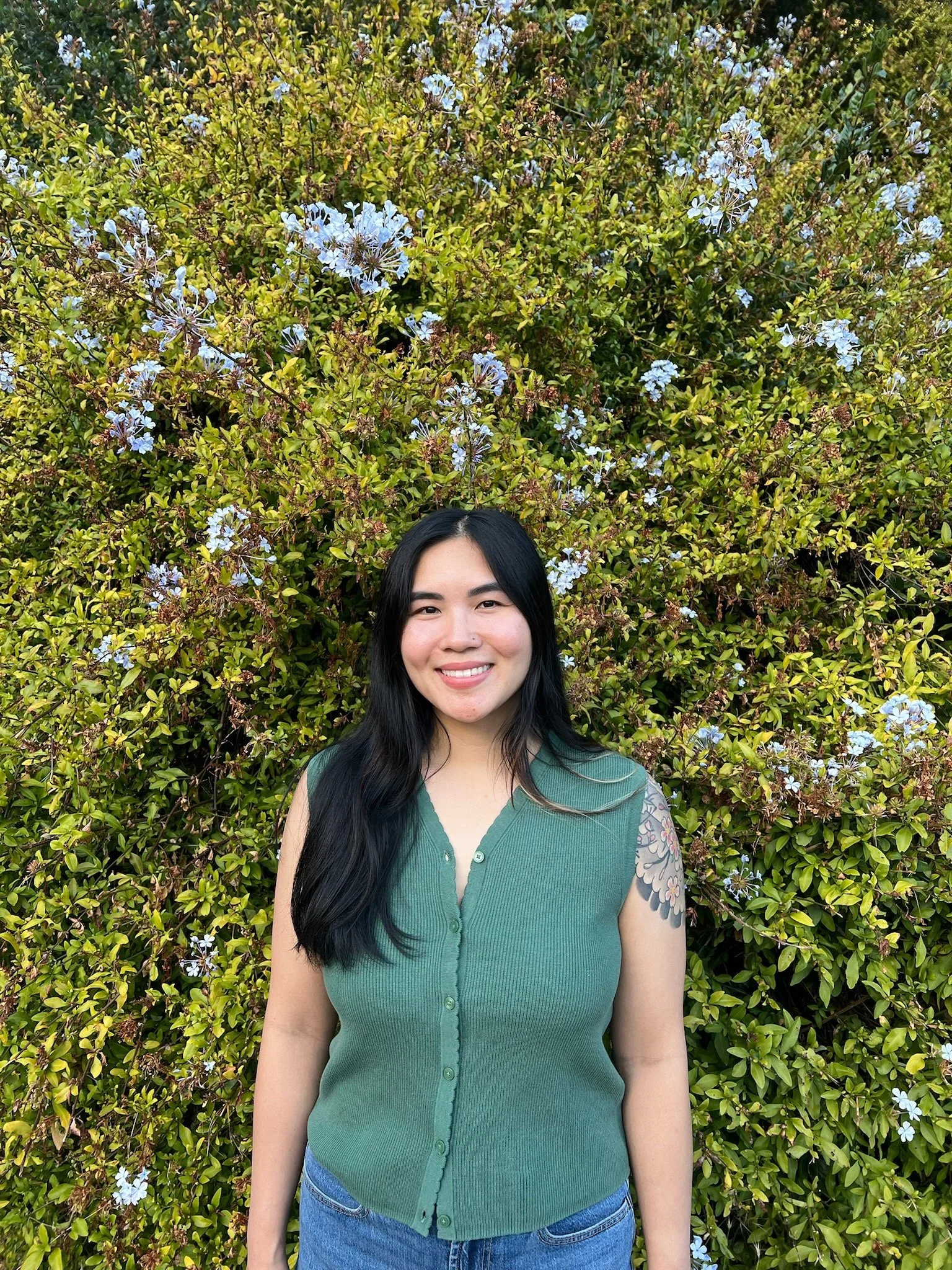 Christina Dinh standing outdoors surrounded by greenery and flowers.