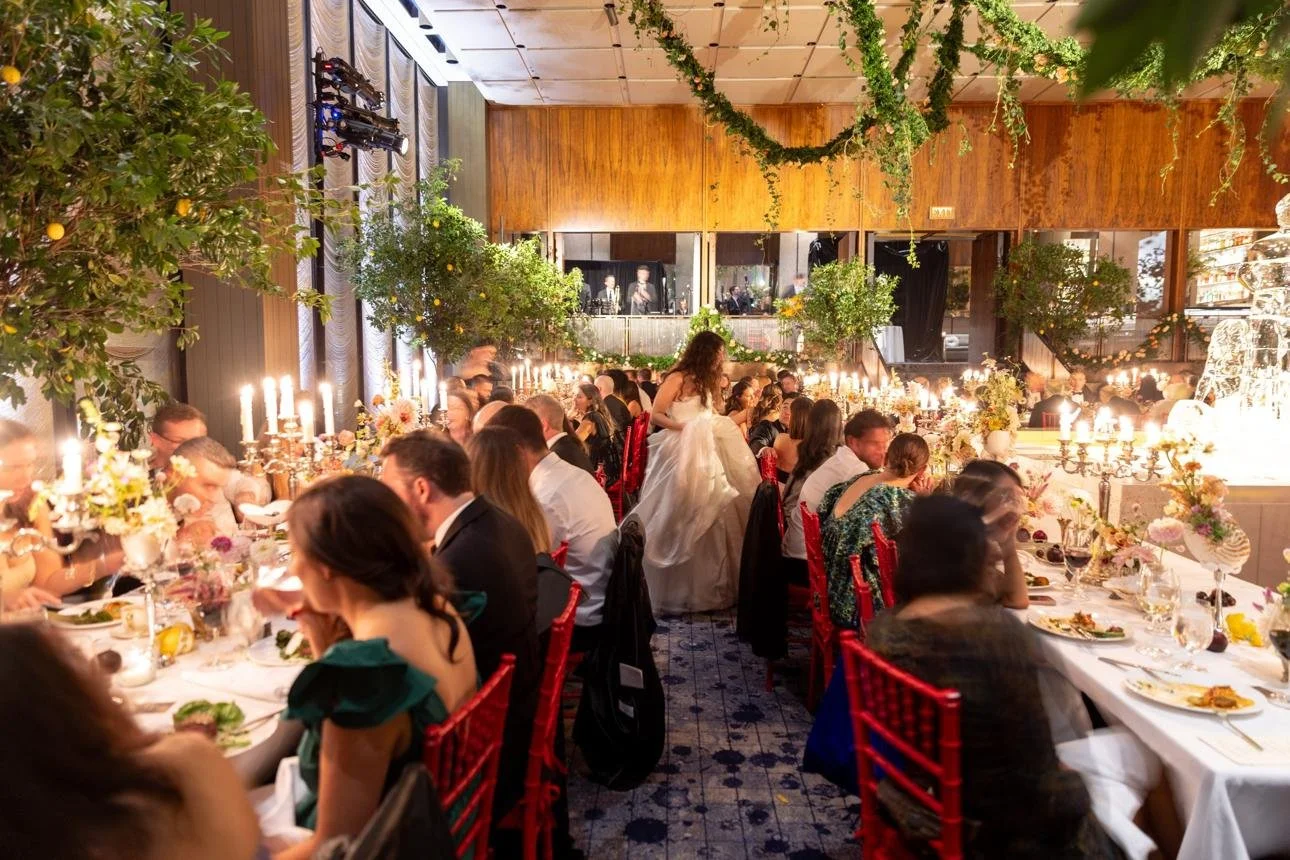 Guests dining at a wedding reception with floral centrepieces and warm festoon lighting