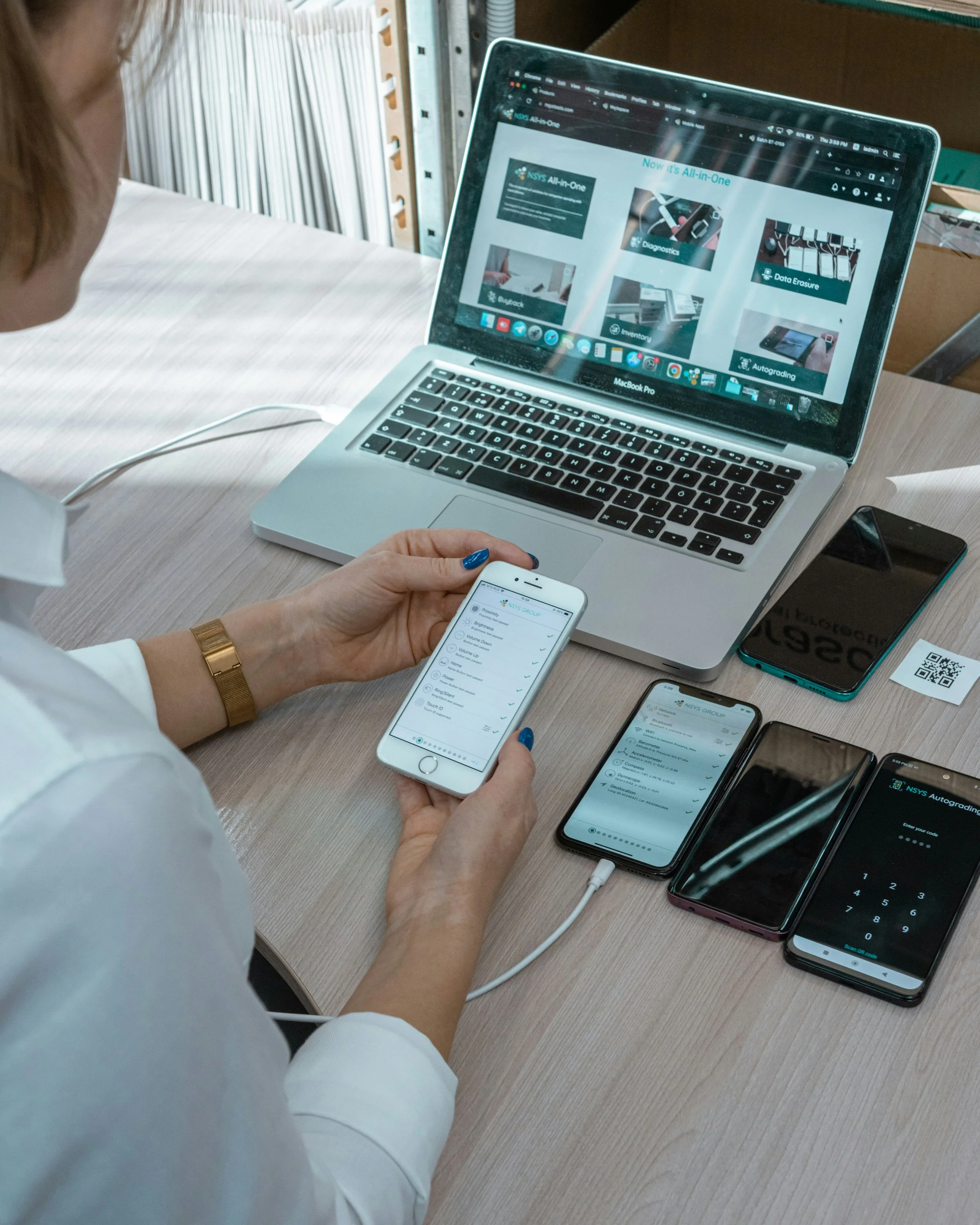 A woman sitting in front of laptop while holding a mobile phone in her hand.