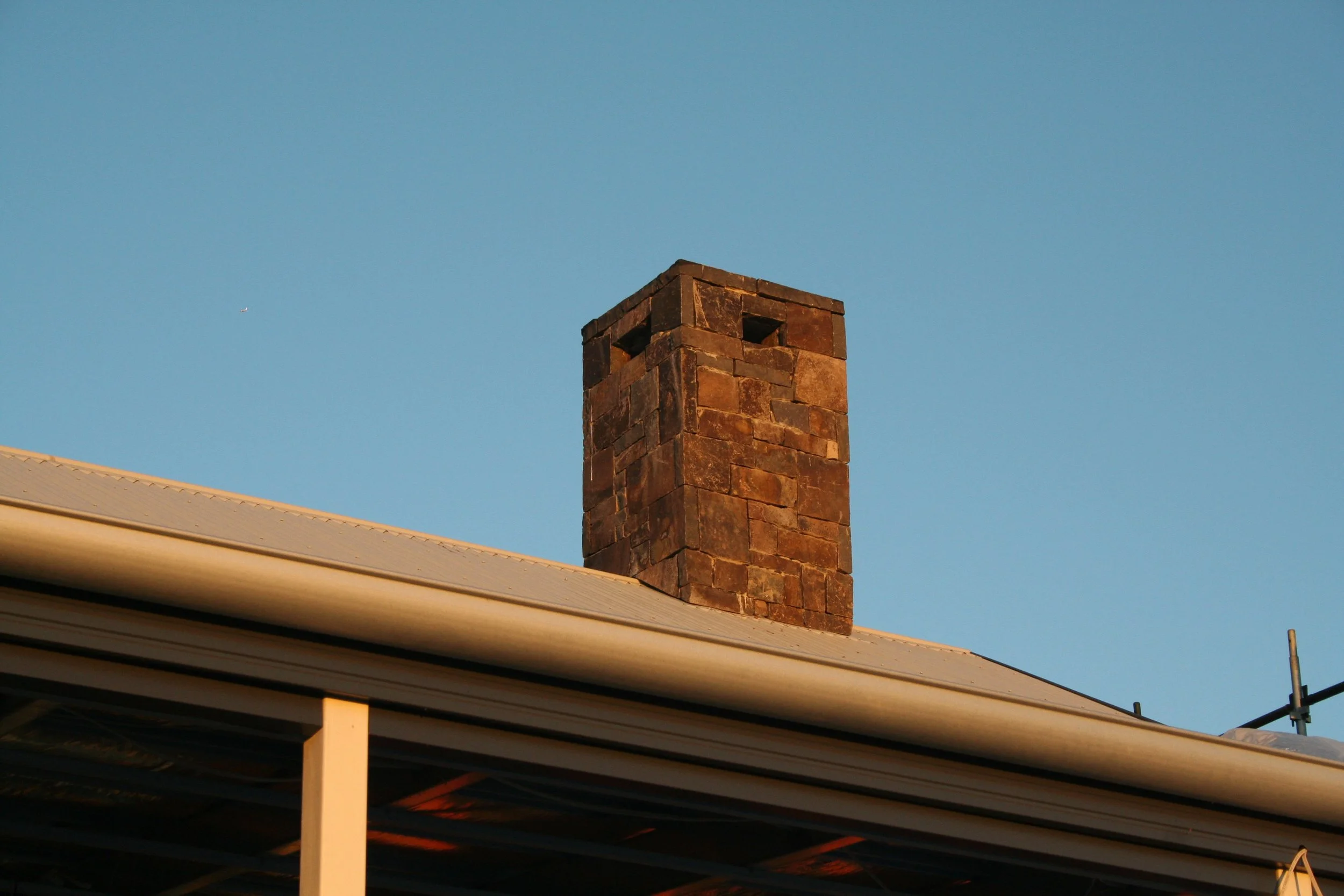 A brick chimney extending from a roof against a clear blue sky.