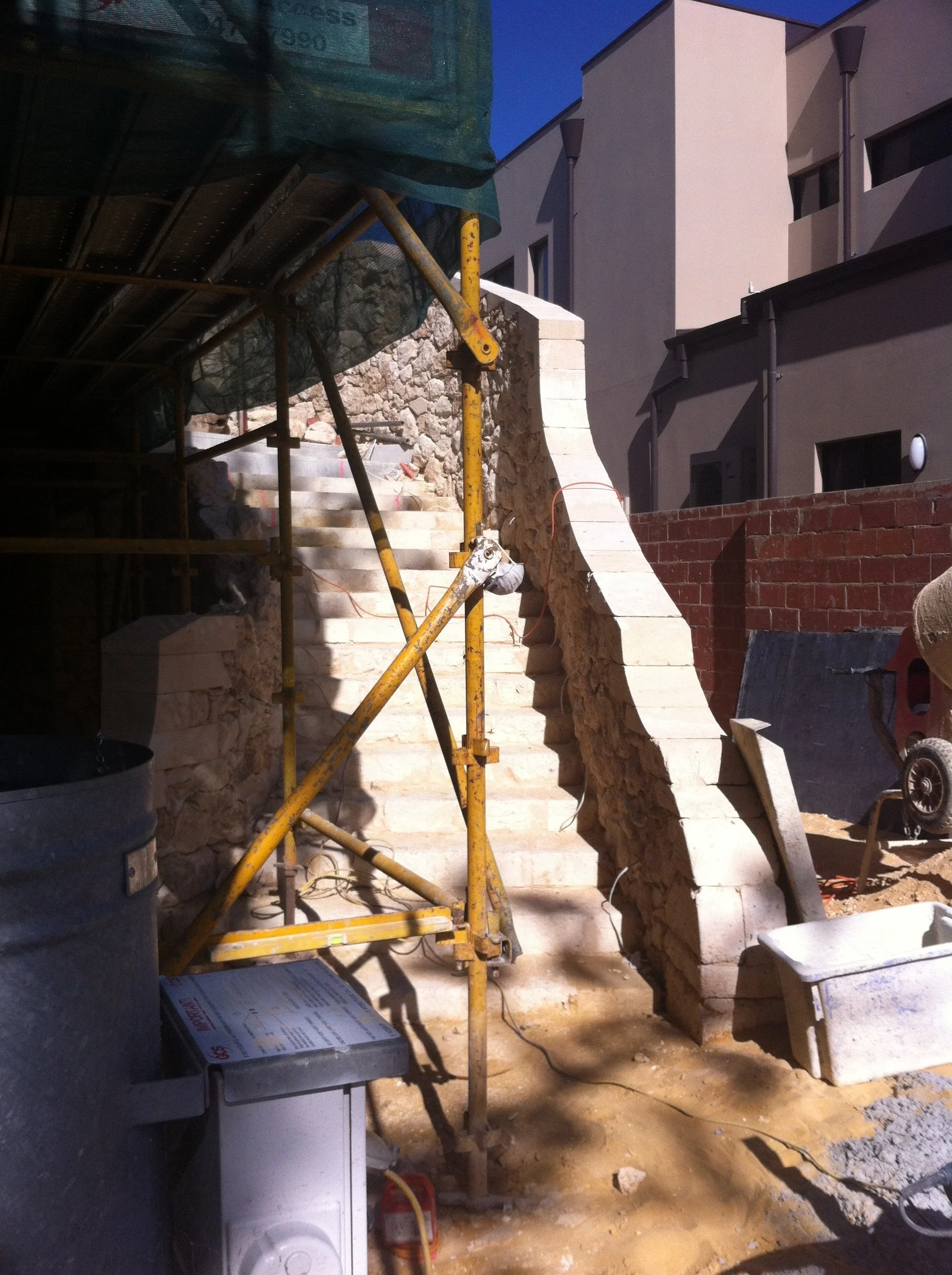 Construction site with stone stairs, scaffolding, building walls, and construction materials during the evening or night.