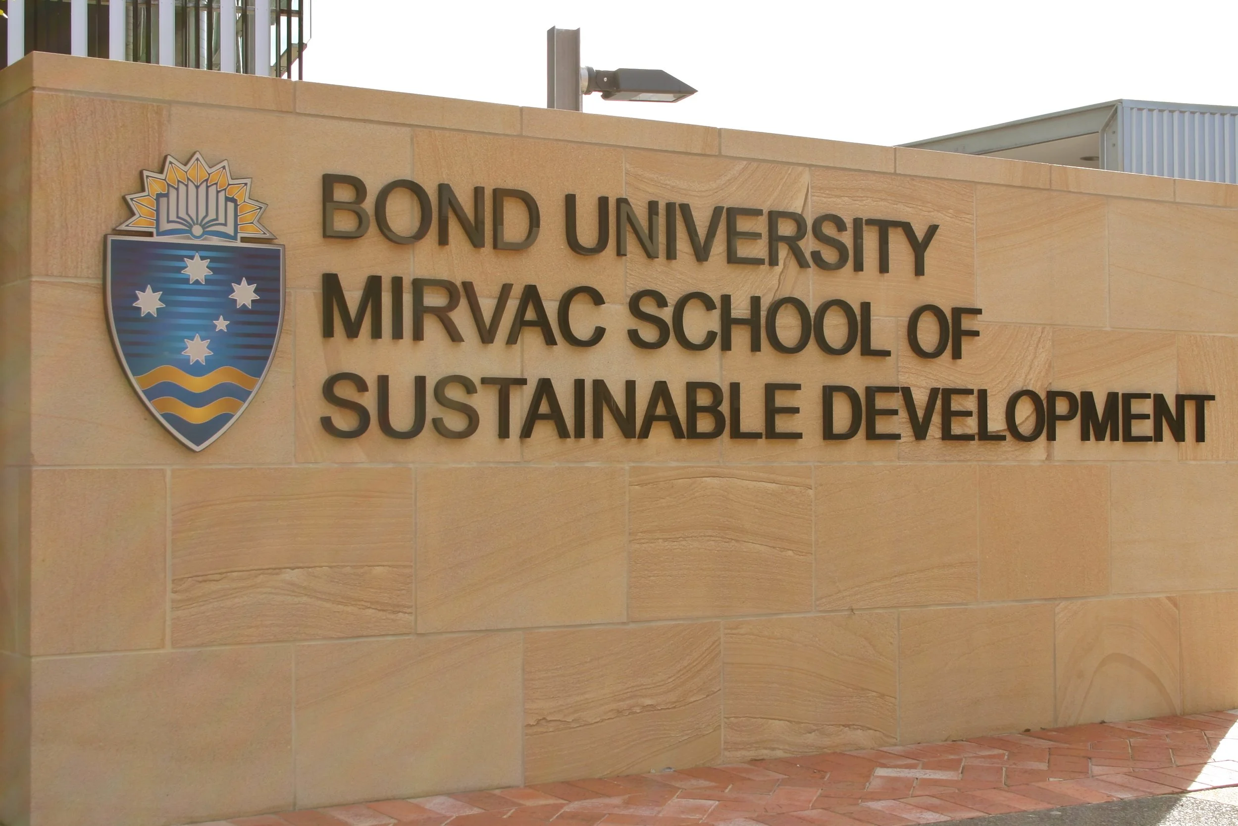 Sign on a beige stone wall displaying Bond University Mirvac School of Sustainable Development logo and name.
