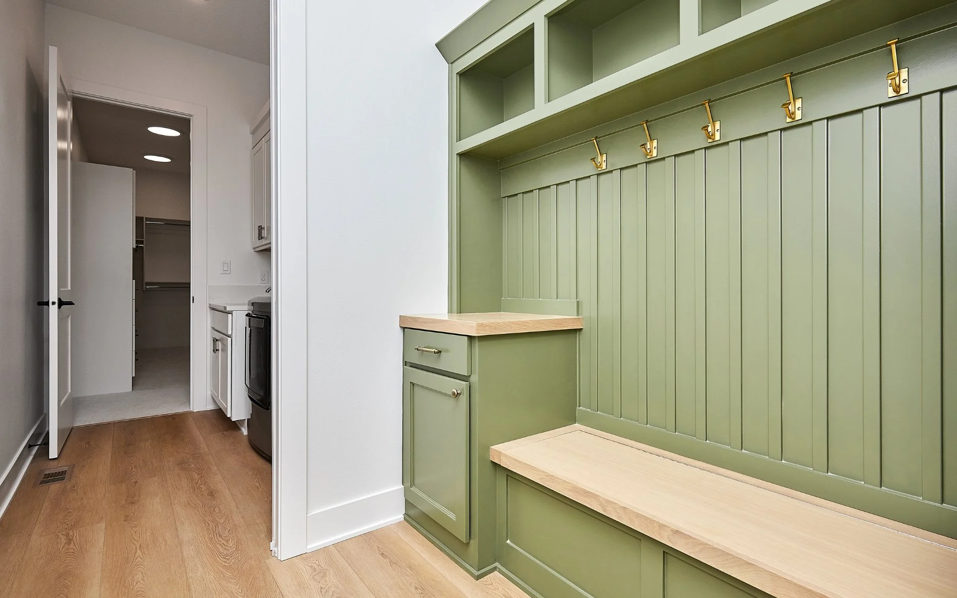custom mudroom with green cabinets wood bench and brass coat hooks