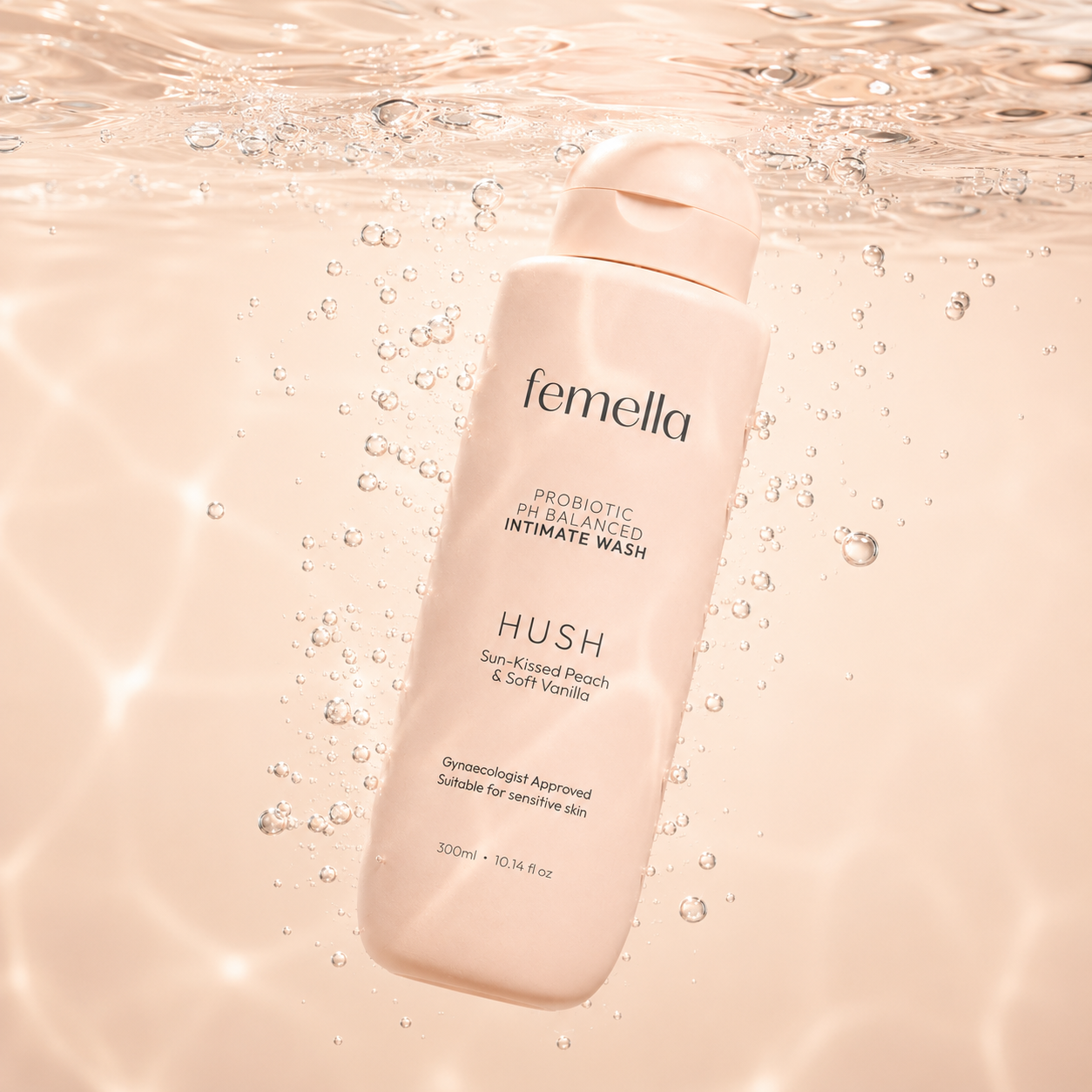 A pink bottle of Femella probiotic pH balanced intimate wash with peach and vanilla scent, floating underwater surrounded by bubbles.
