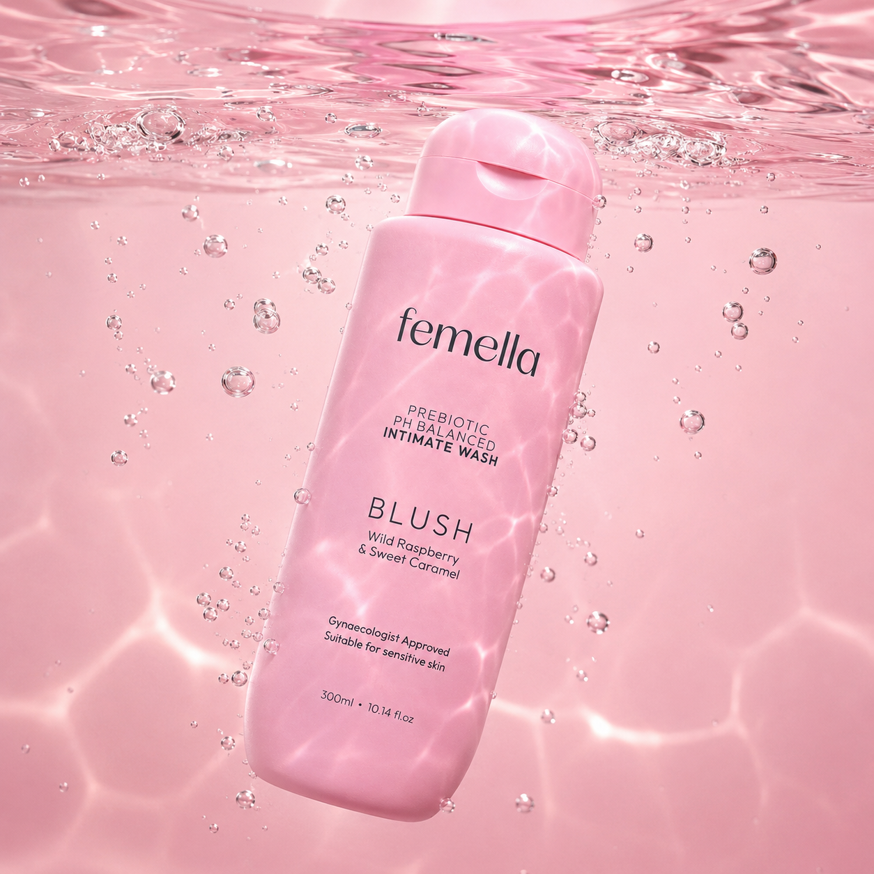 A pink bottle of Femella intimate wash submerged in water with bubbles, labels read 'Prebiotic PH Balanced Intimate Wash Blush Wild Raspberry & Sweet Caramel'.