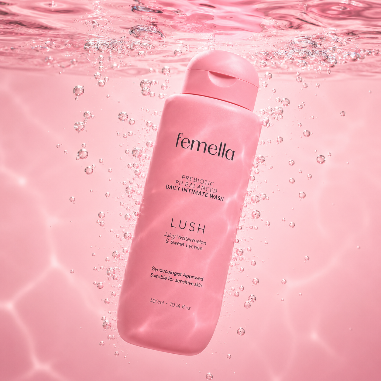 A pink bottle of Femella Daily Intimate Wash submerged in water with bubbles, featuring watermelon and lychee flavor, on a pink background.