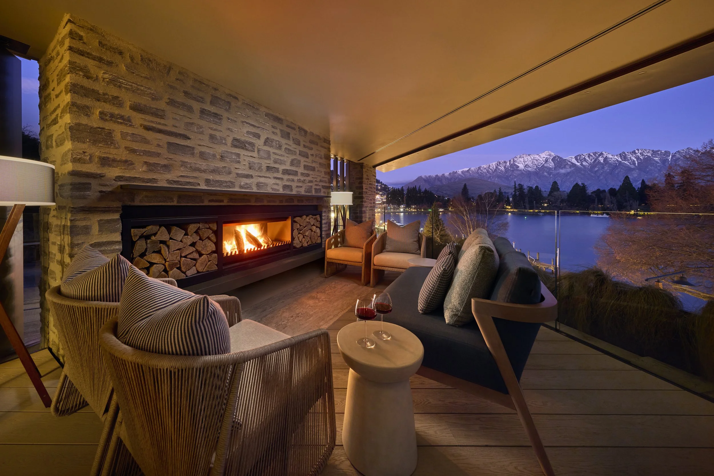 Living room with fireplace, armchairs, and view of snow-capped mountains and a lake during dusk.