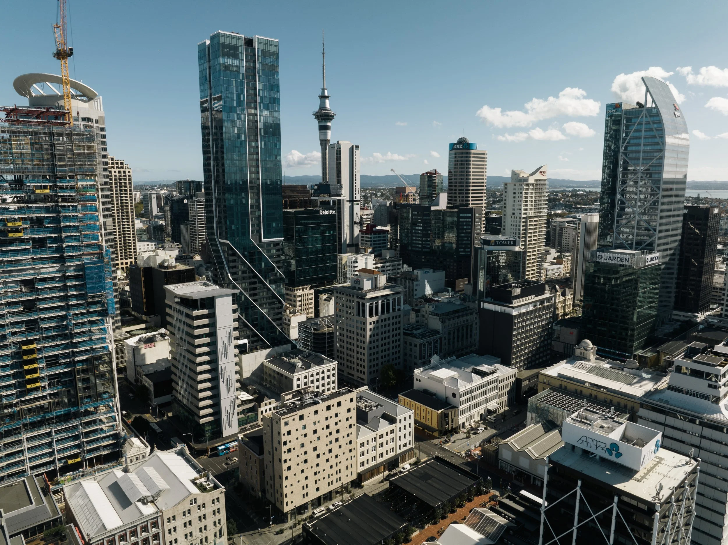 A city skyline with tall modern glass skyscrapers, including Sky Tower in Auckland, New Zealand, under a clear blue sky.
