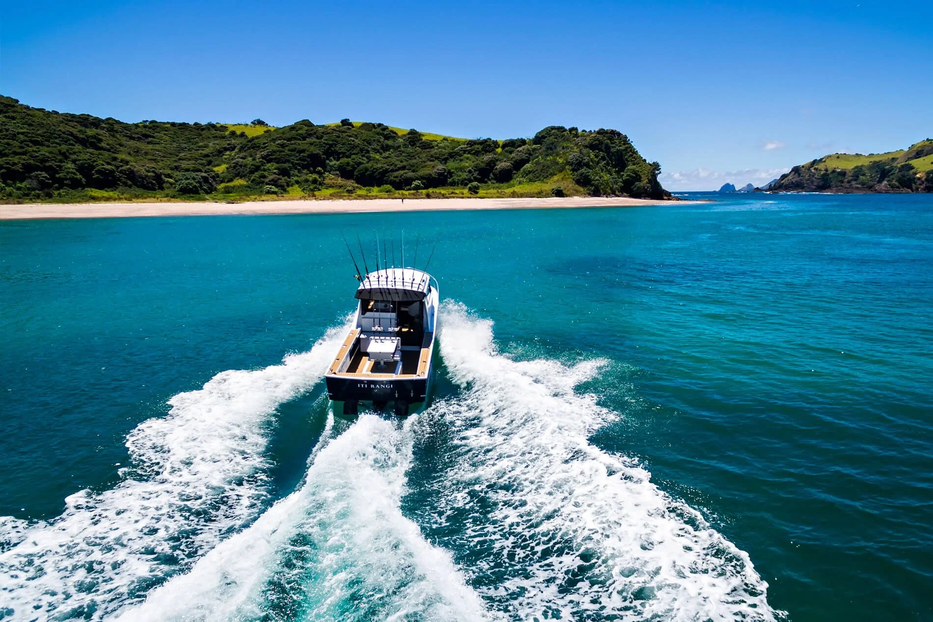 Motorboat speeding through turquoise water near green hilly coastline under blue sky.