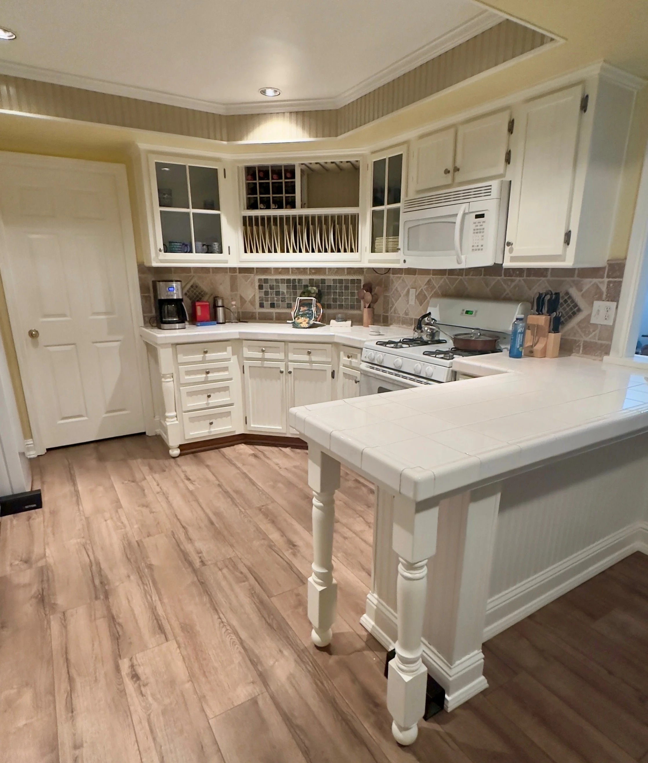 Kitchen with beige cabinetry, microwave, oven, and a white kitchen island. Wood flooring, tiled backsplash, and dish rack above the counter.