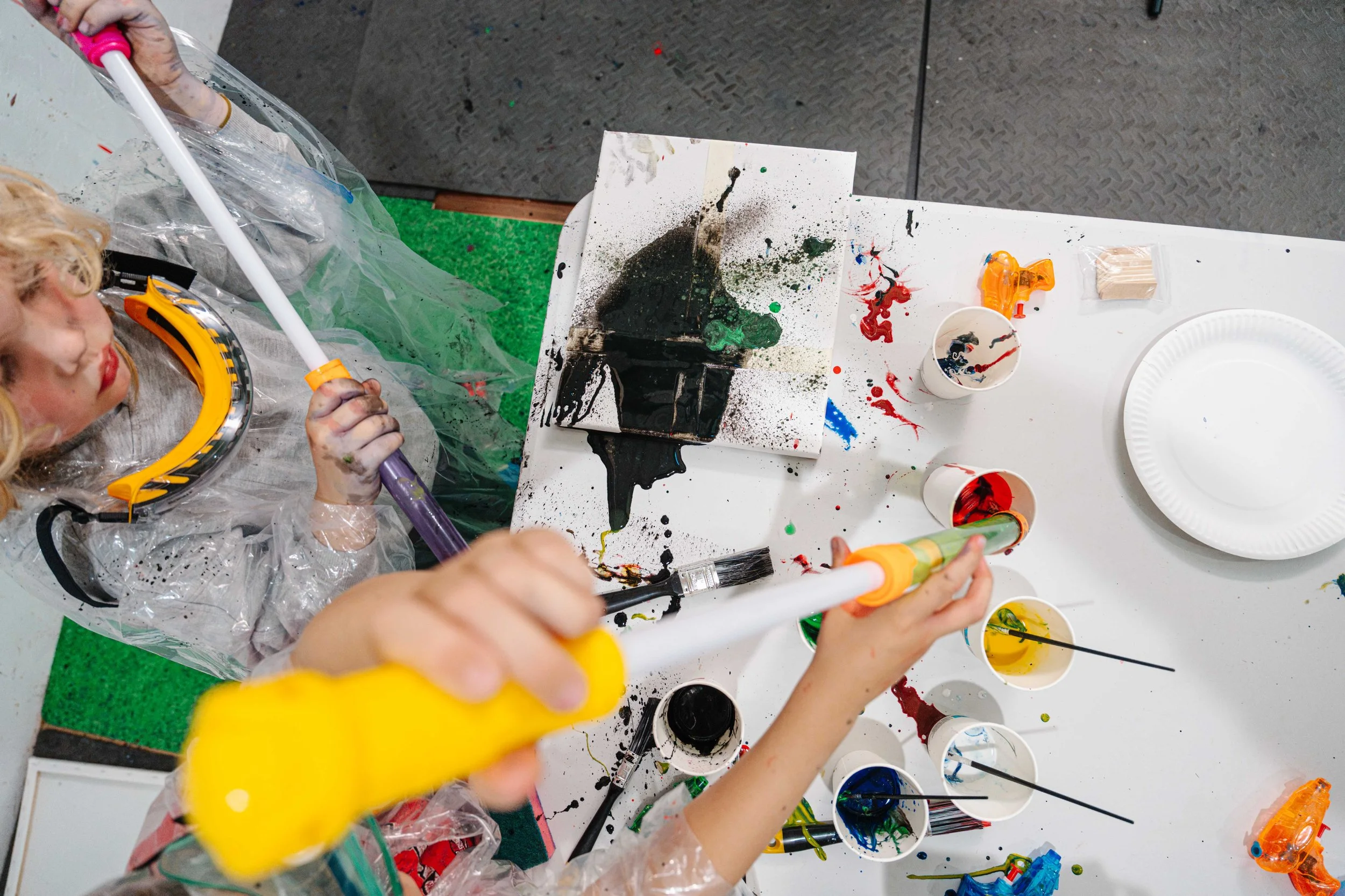 Children engaging in a messy arts and crafts activity, using paint, glue, and various art supplies on a white table.