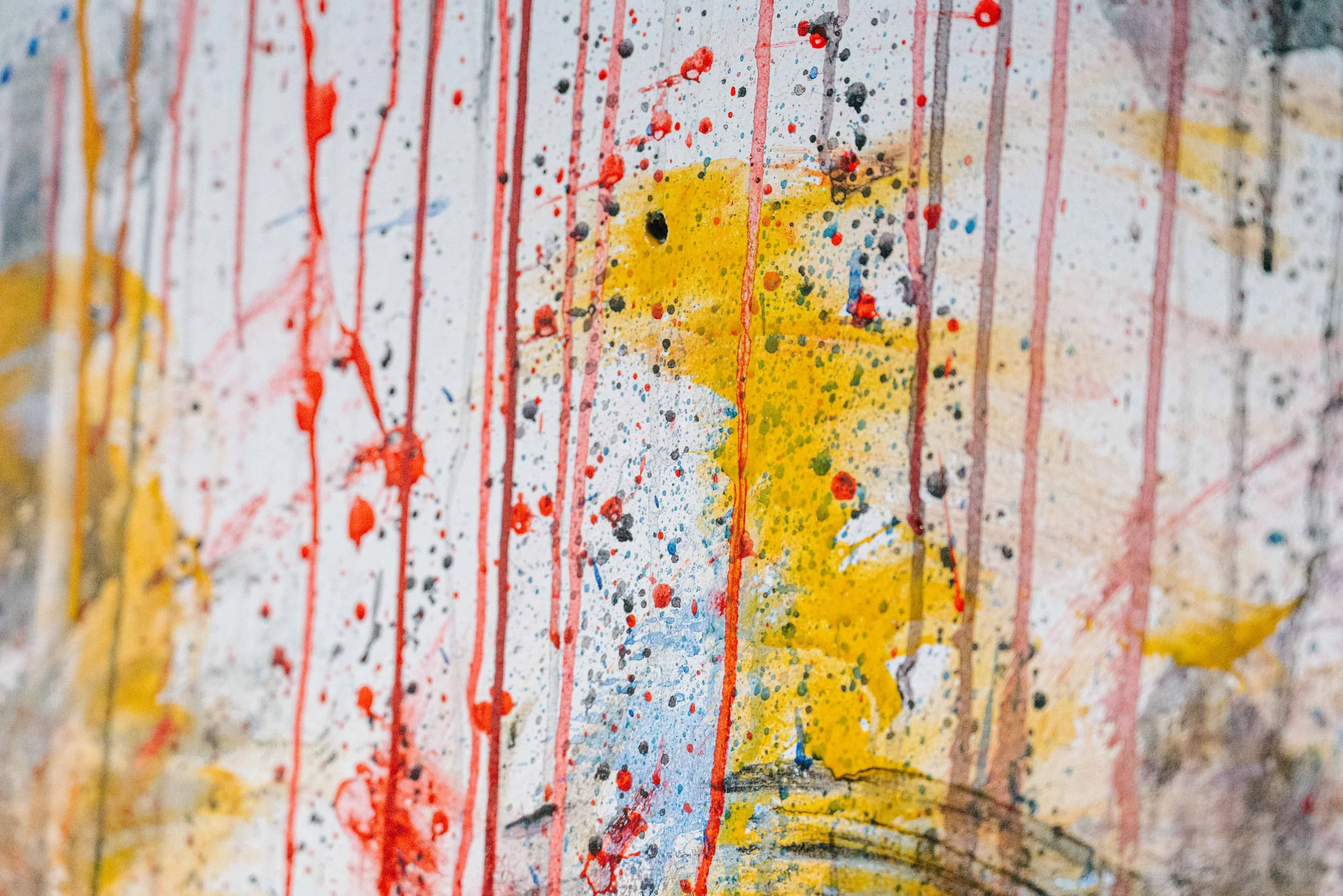 Close-up of a wall with colorful abstract splatters and paint drips, featuring red, yellow, black, and blue paint.