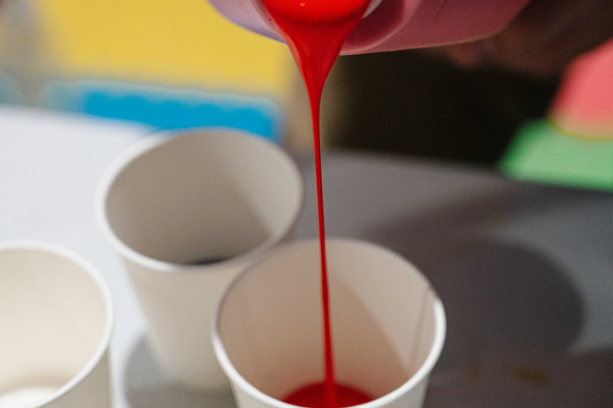 Close-up of red liquid being poured into a white test tube, with other test tubes in the background.