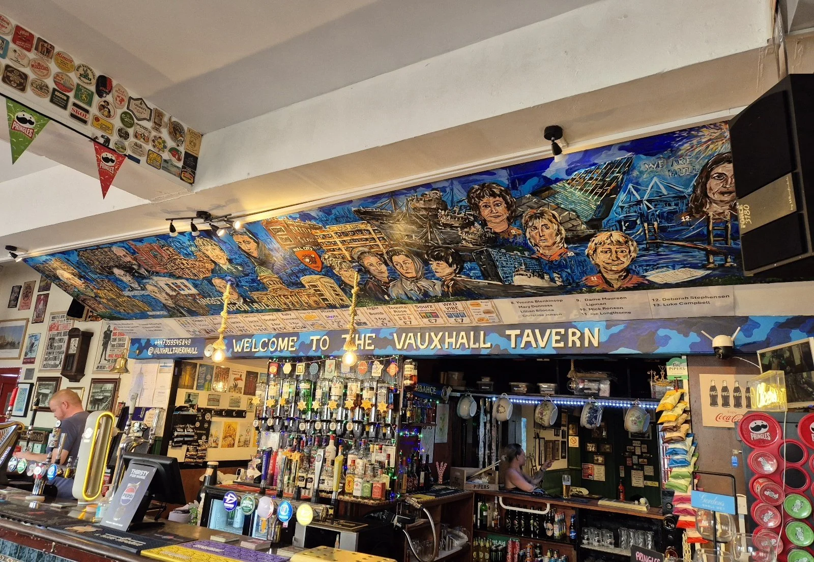 Interior of Vauxhall Tavern with colorful mural and bar area, decorated with various memorabilia and signs.