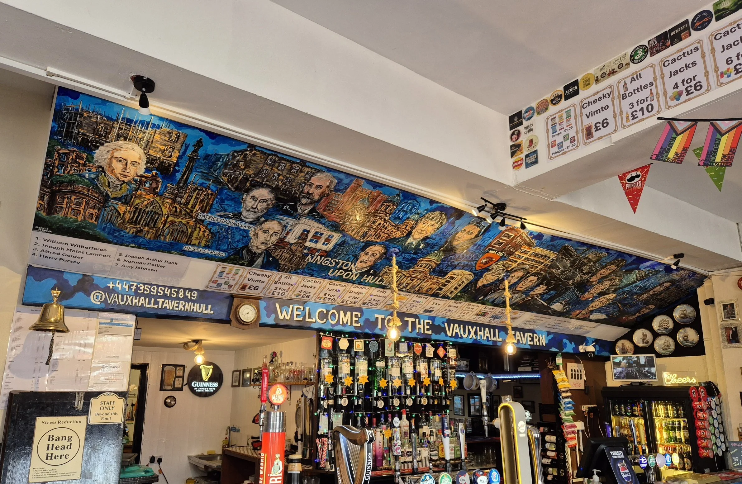 Colorful wall mural of historical figures and buildings, with signs displaying menu items and prices in a pub or cafe.
