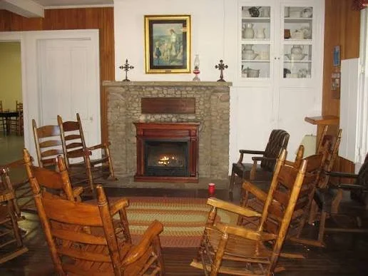 Living room with a stone fireplace, wooden rocking chairs arranged in a circle, a framed painting above the fireplace, and built-in white shelves.