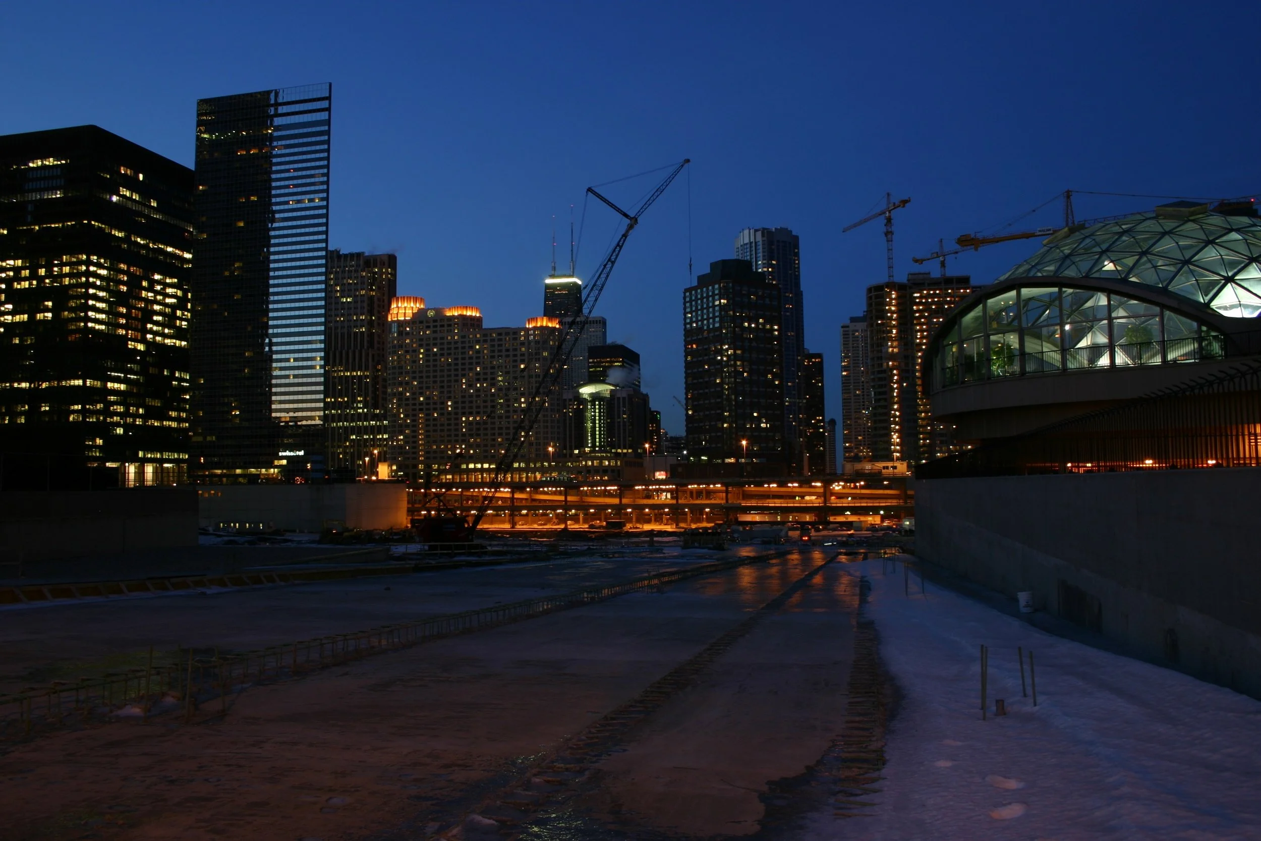 The Chicago skyline at blue hour, lit office towers and a glass dome reflected in the river below.