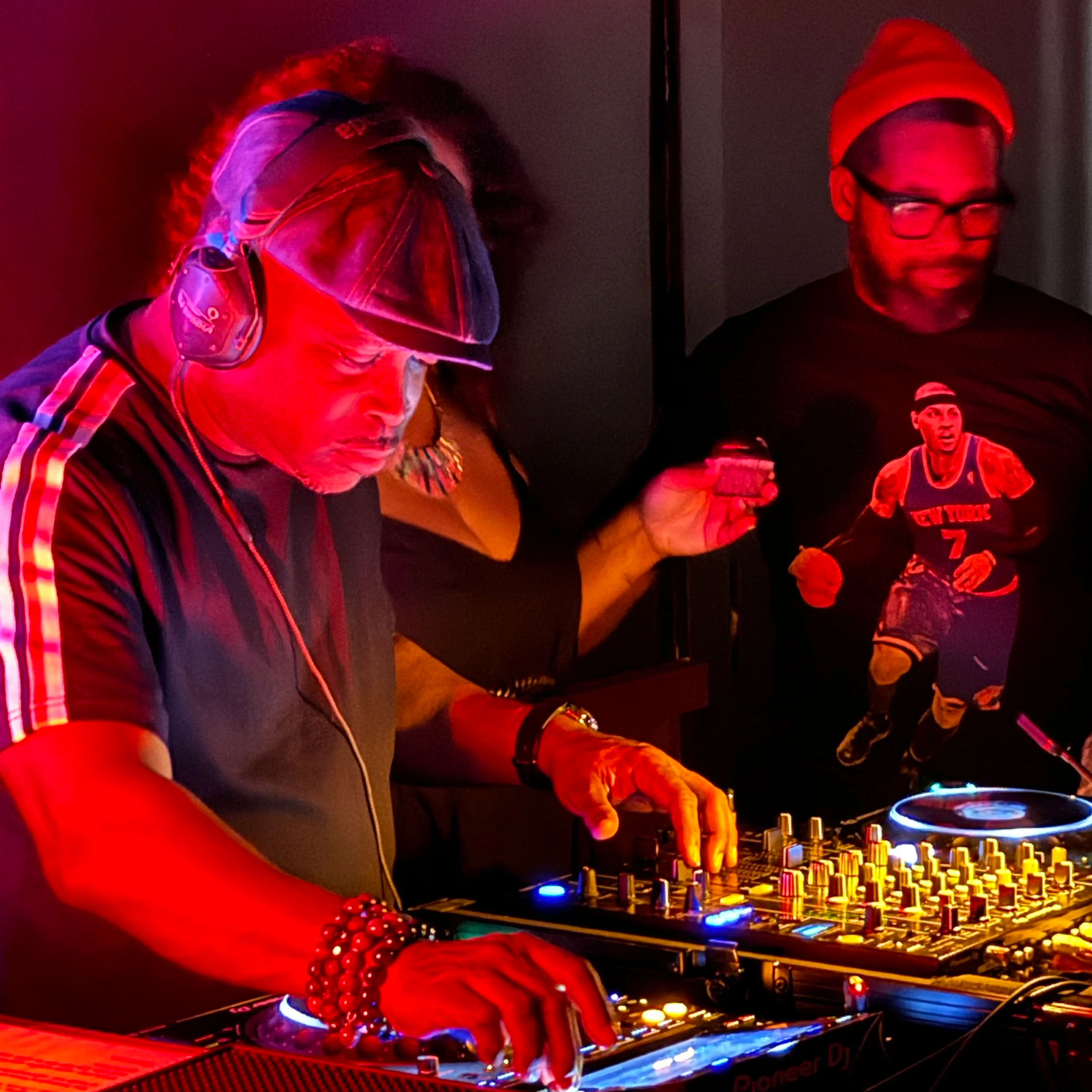 The legendary DJ Spinna, bathed in a red light,  playing on CDJs