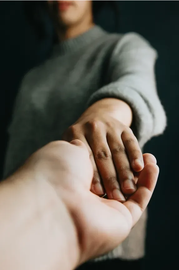 Person in gray sweater holding hands with another person against a dark background.