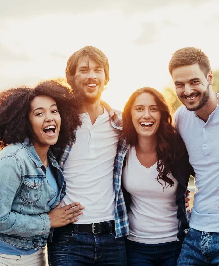 Group of four young adults smiling and enjoying outdoors at sunset.