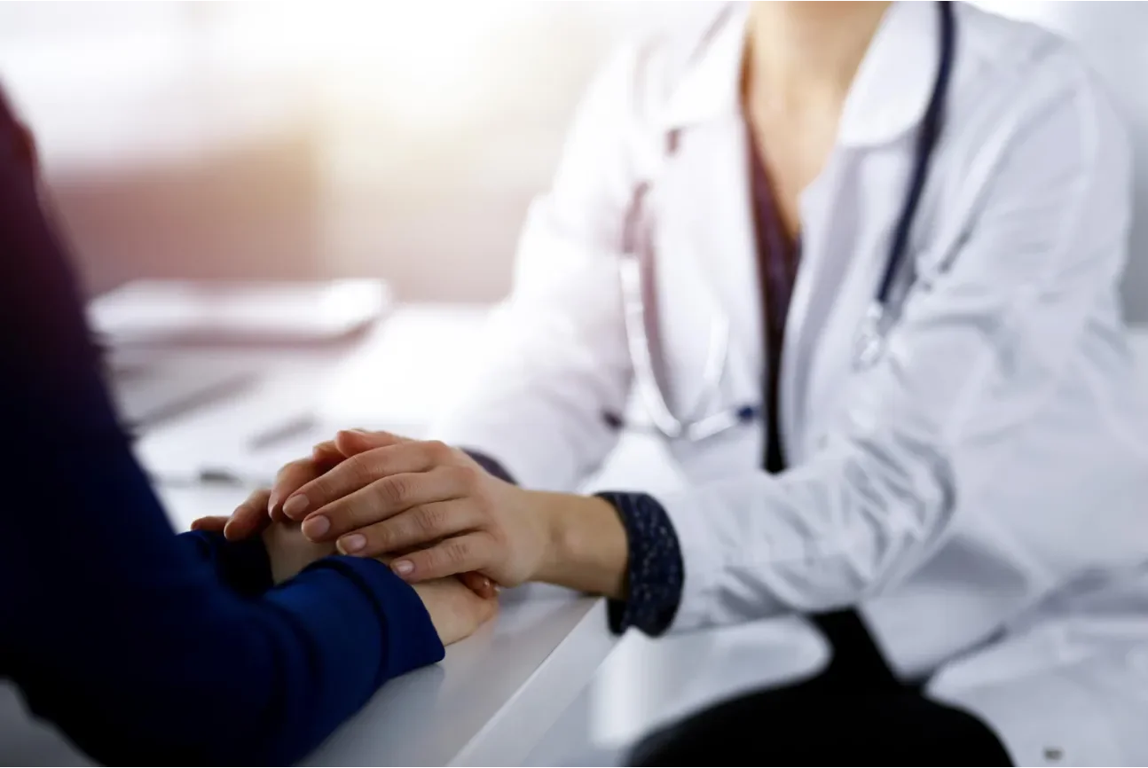 Doctor holding patient's hand during consultation in an office setting.