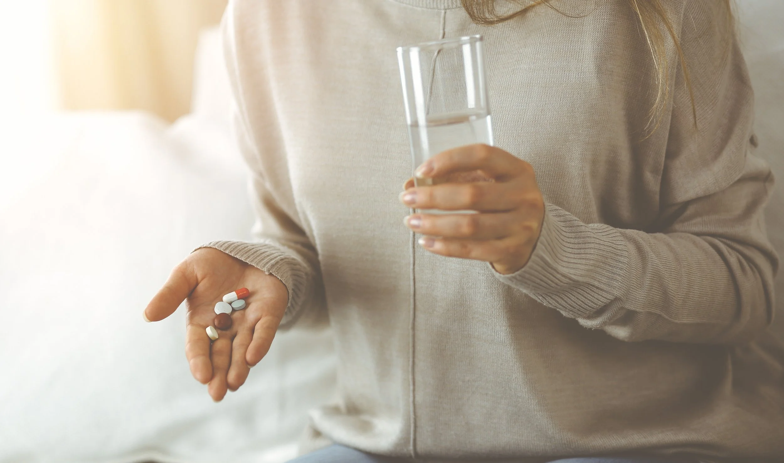 A person holding pills in one hand and a glass of water in the other.
