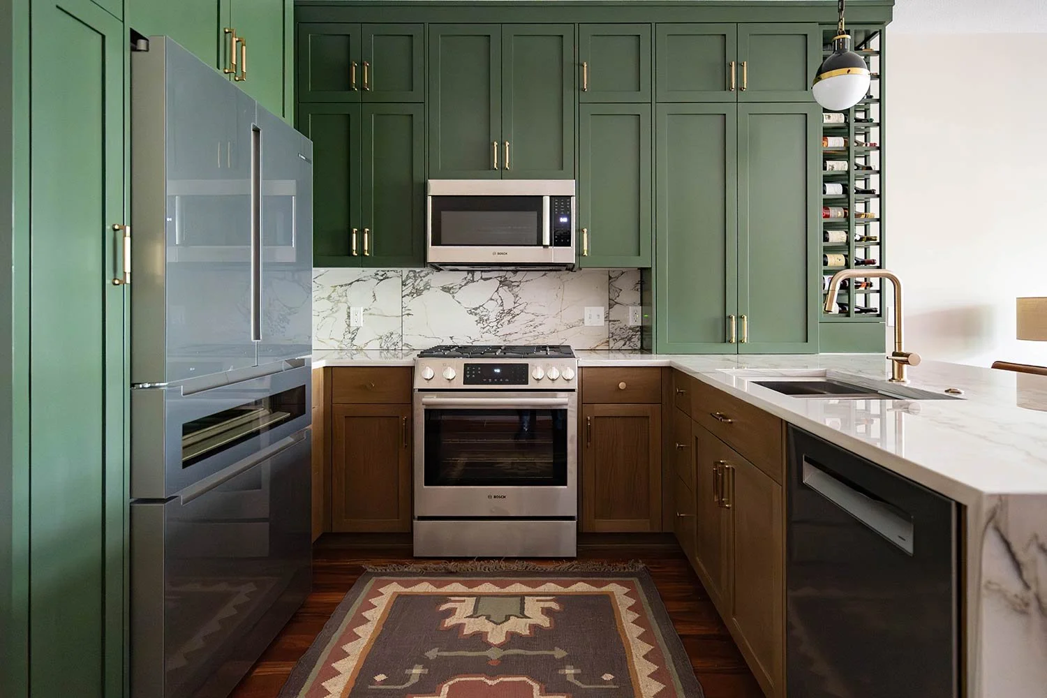 Modern kitchen with green and wood cabinets, marble countertops, stainless steel appliances, and a wine rack.