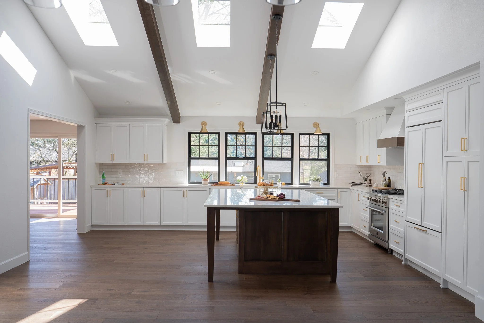 Modern kitchen with white cabinets, a center island with a wooden base, black window frames, and a large skylight ceiling.