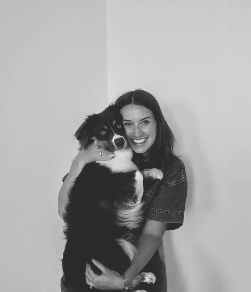 A smiling woman holding a large black and white dog indoors.