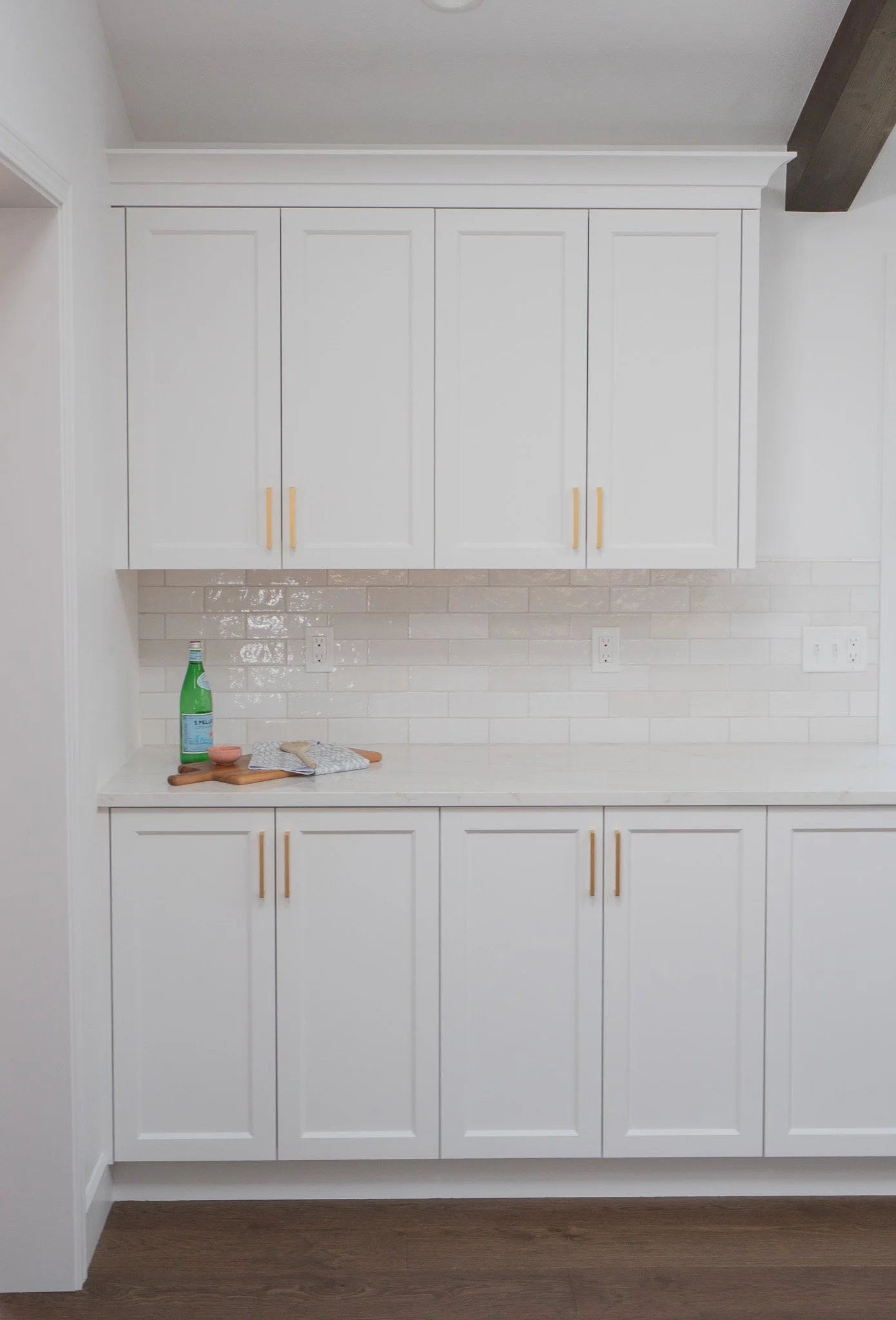Kitchen with white cabinets, a white tile backsplash, and wood flooring. Items on the countertop include a green soda bottle, a small bowl, a cloth, and a wooden utensil.