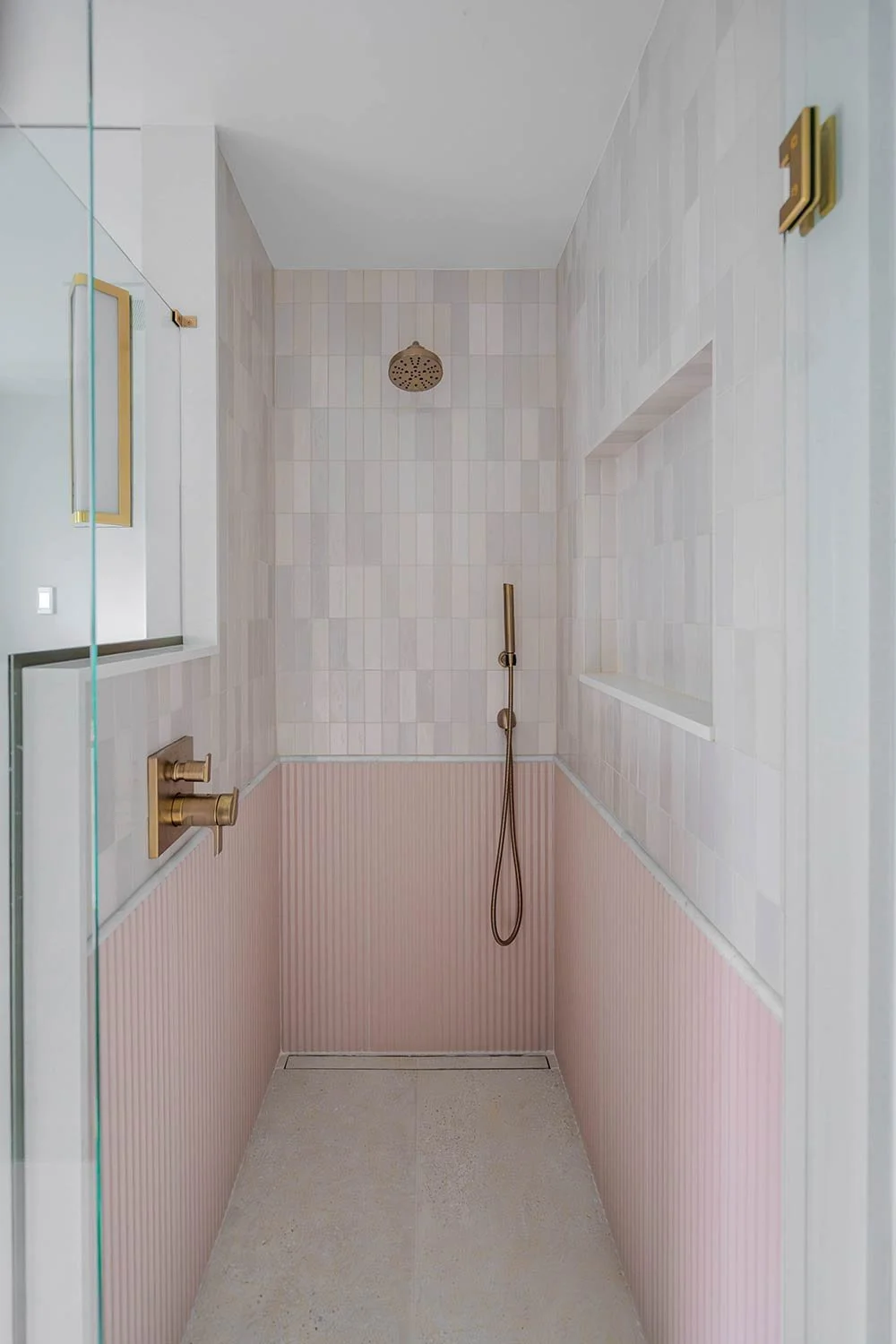 Modern shower with pink and beige tiles, gold fixtures, and a glass partition.