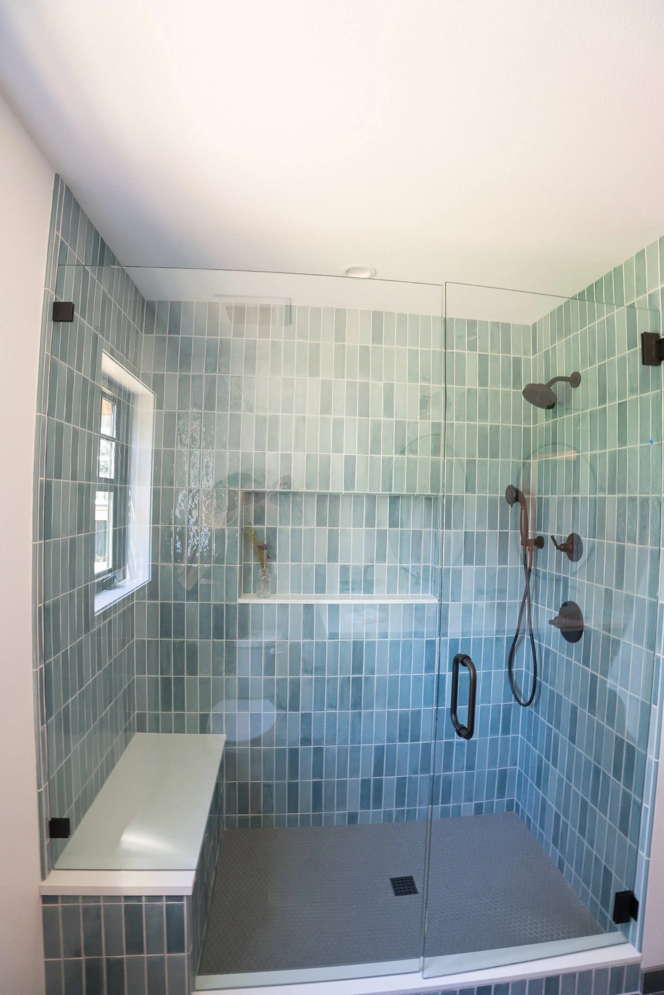 Modern walk-in shower with glass door, blue tiles, black showerhead, and built-in bench.