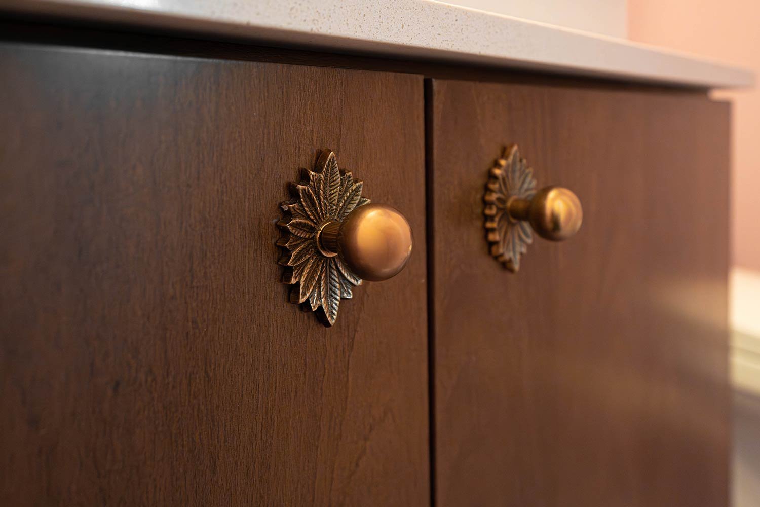Close-up of dark wooden cabinet doors with decorative brass handles shaped like leaves and knobs.