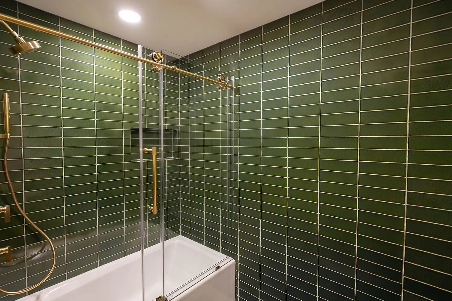 Green tiled bathroom shower with glass door, gold fixtures, and a built-in shelf.